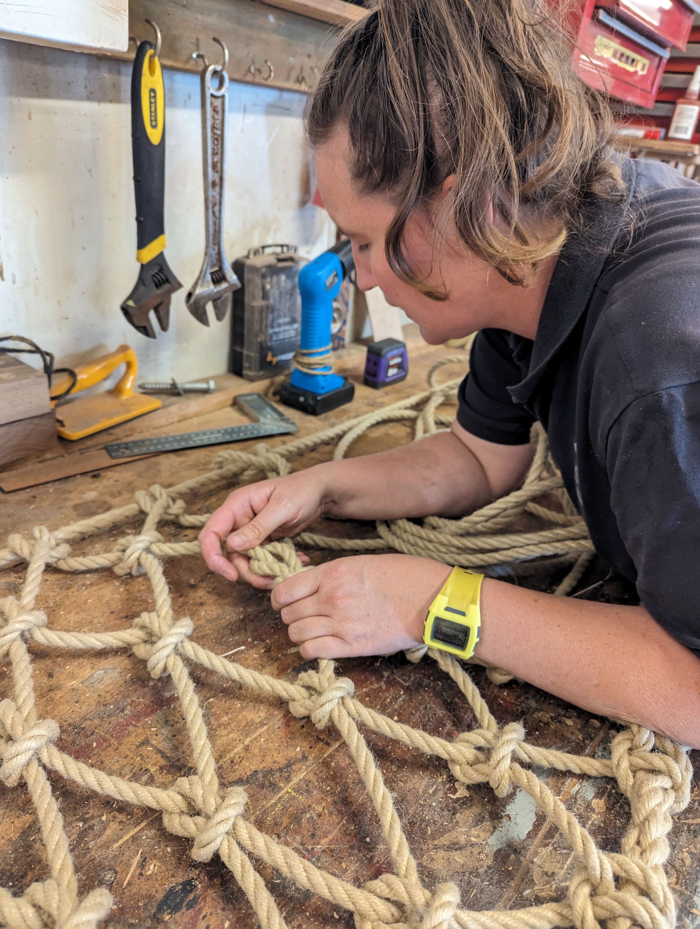 Photo of a woman tying tan coloured ropes together in a grid with diamond shaped holes.