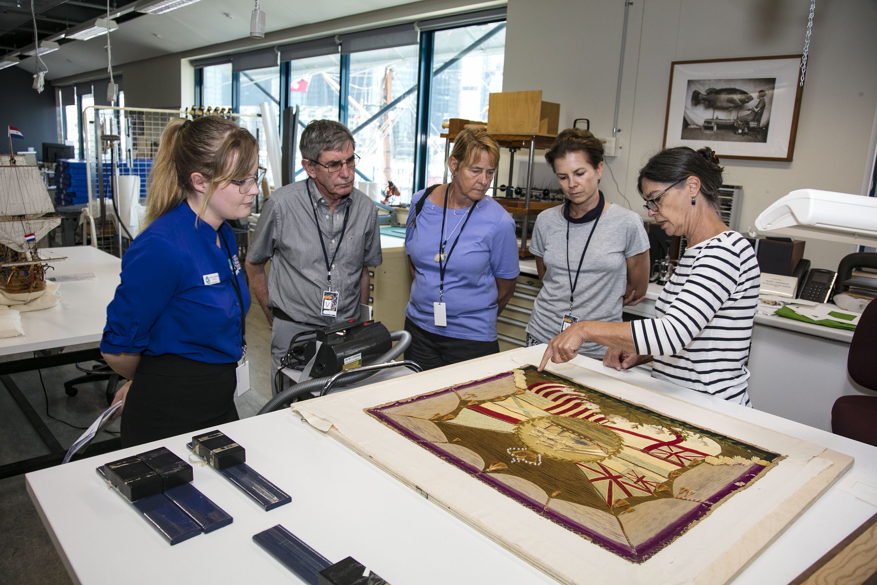 Photo showing 5 people looking at a table featuring an artwork in a conservation lab. 