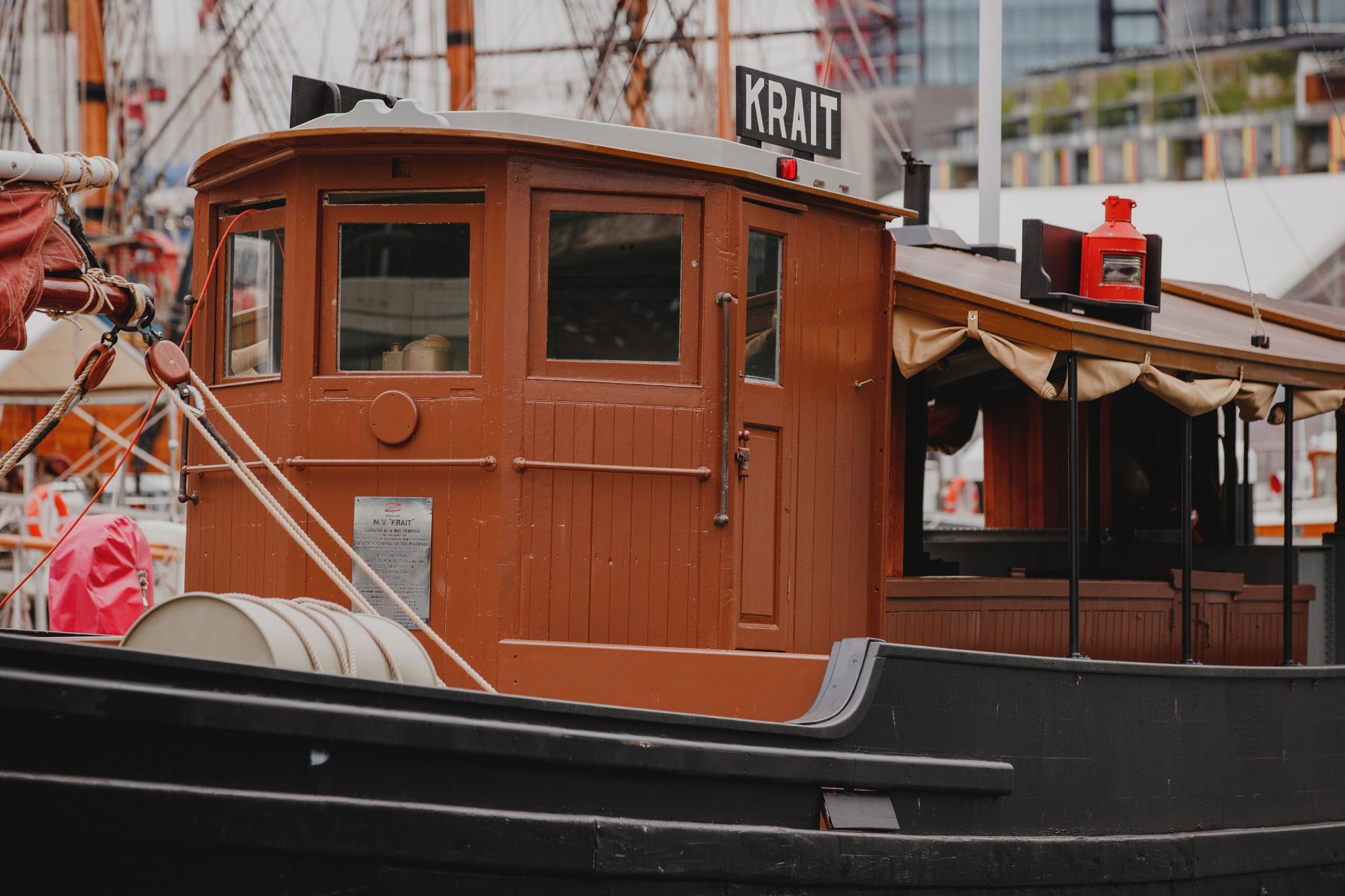 Close up photo of a wooden fishing boat, painted brown with glass windows. A black sign on the roof says "KRAIT" in white letters