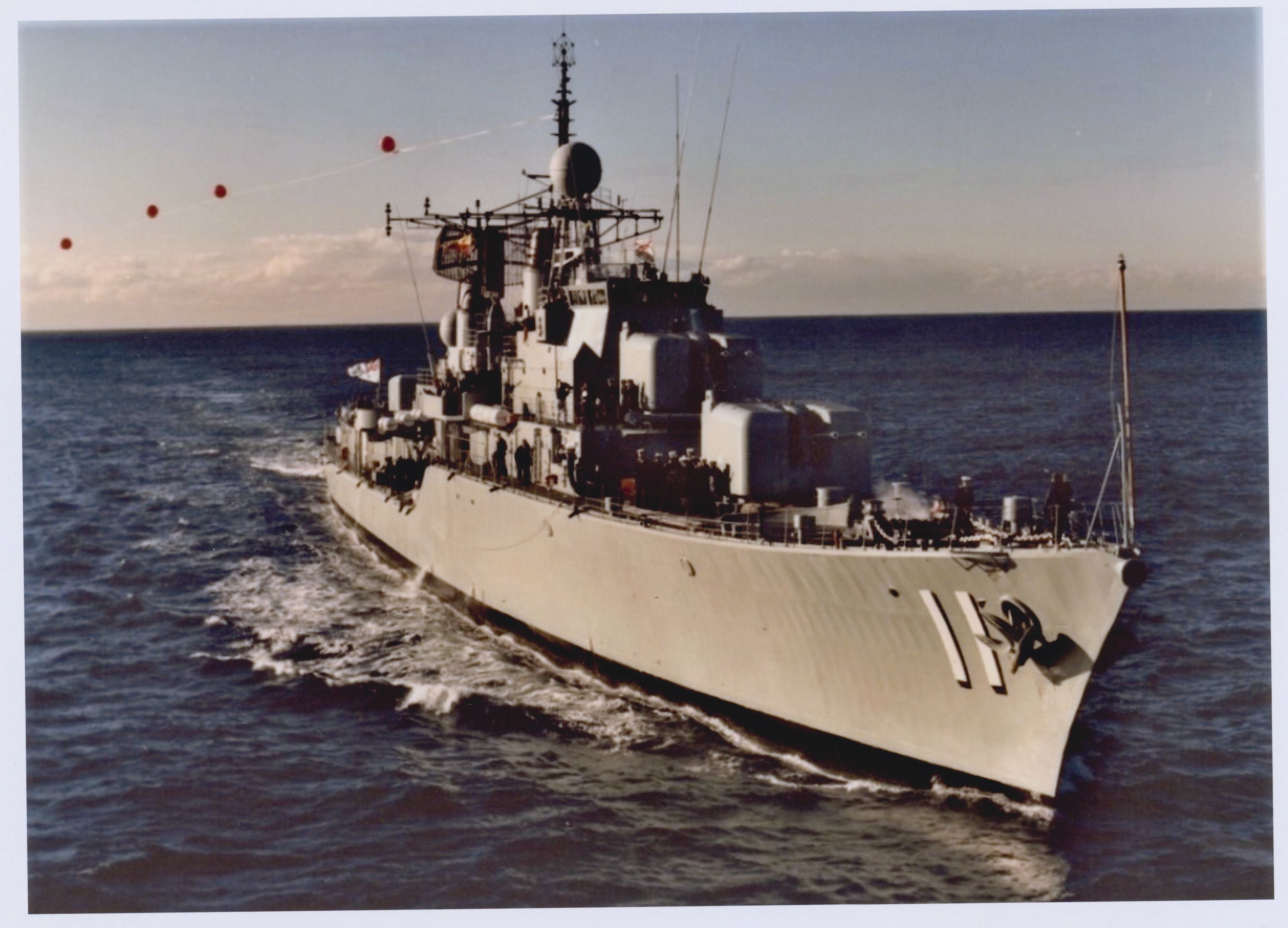 Old colour photo of a grey navy destroyer sailing towards the viewer, slightly to the right 