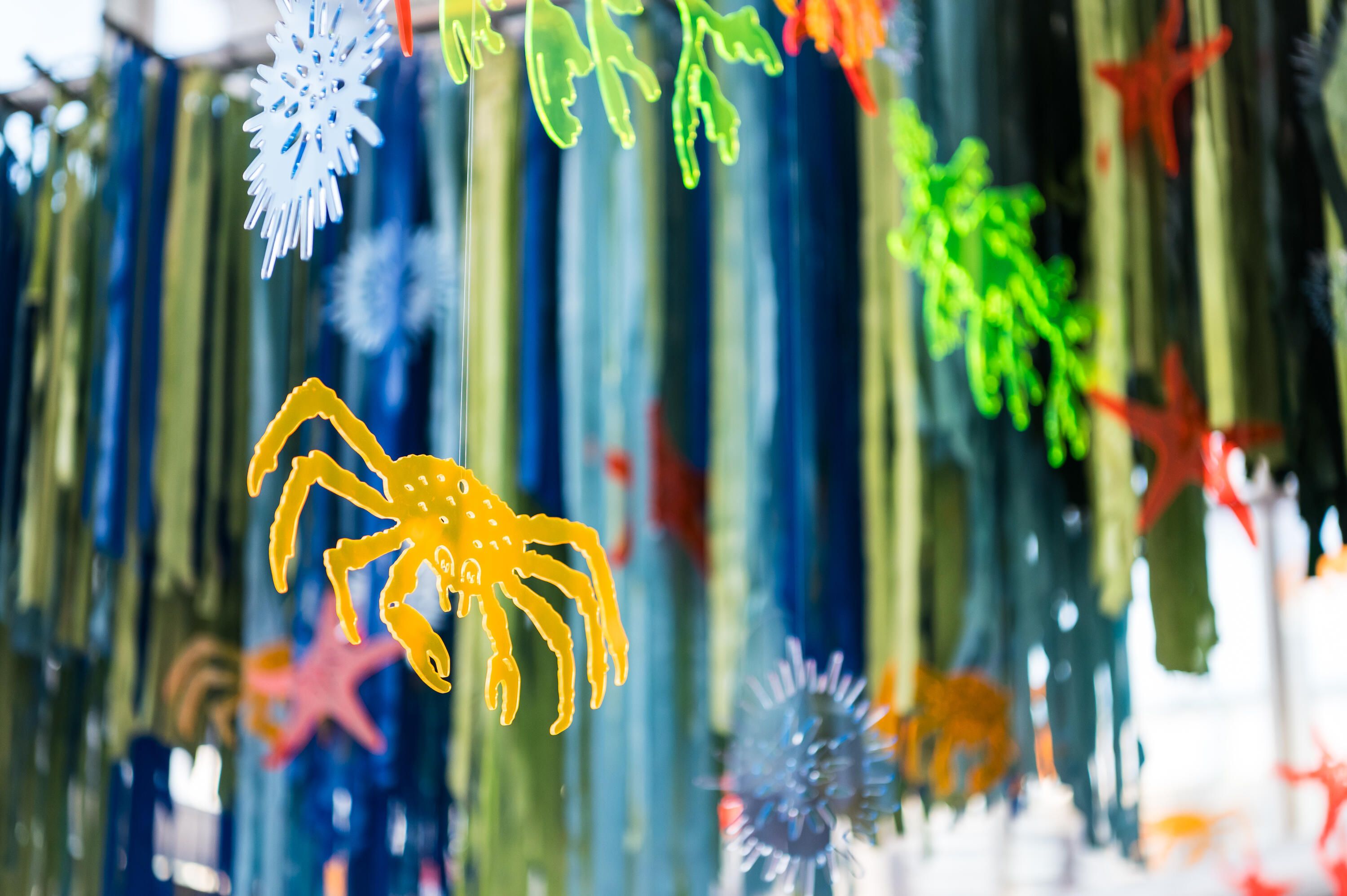 Photo taken of decorations; colourful plastic shapes of seahorses and other sea creatures hanging from a ceiling with blue and green streamers. 
