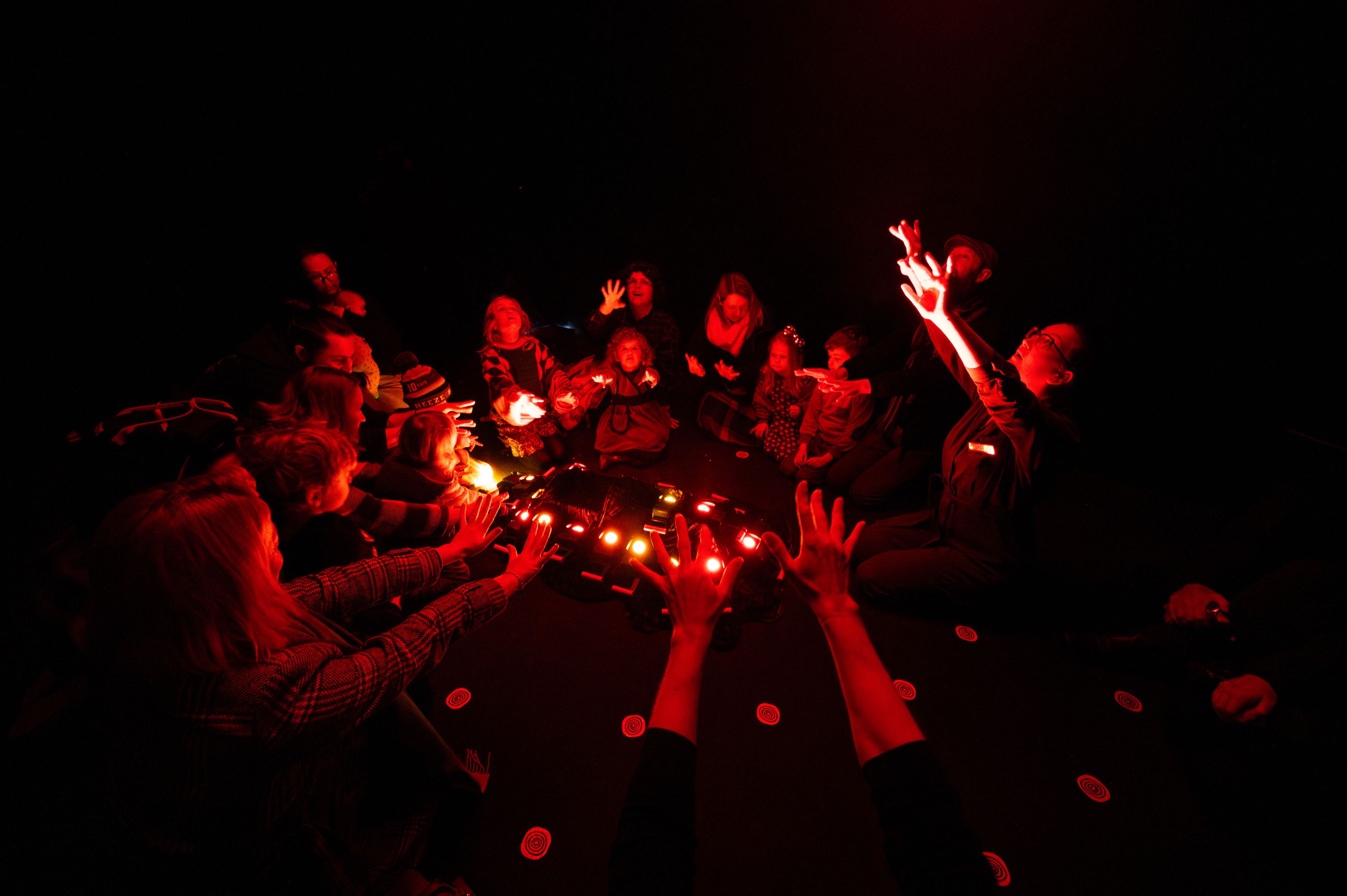 children and adults holding their hands up in a circle with red light