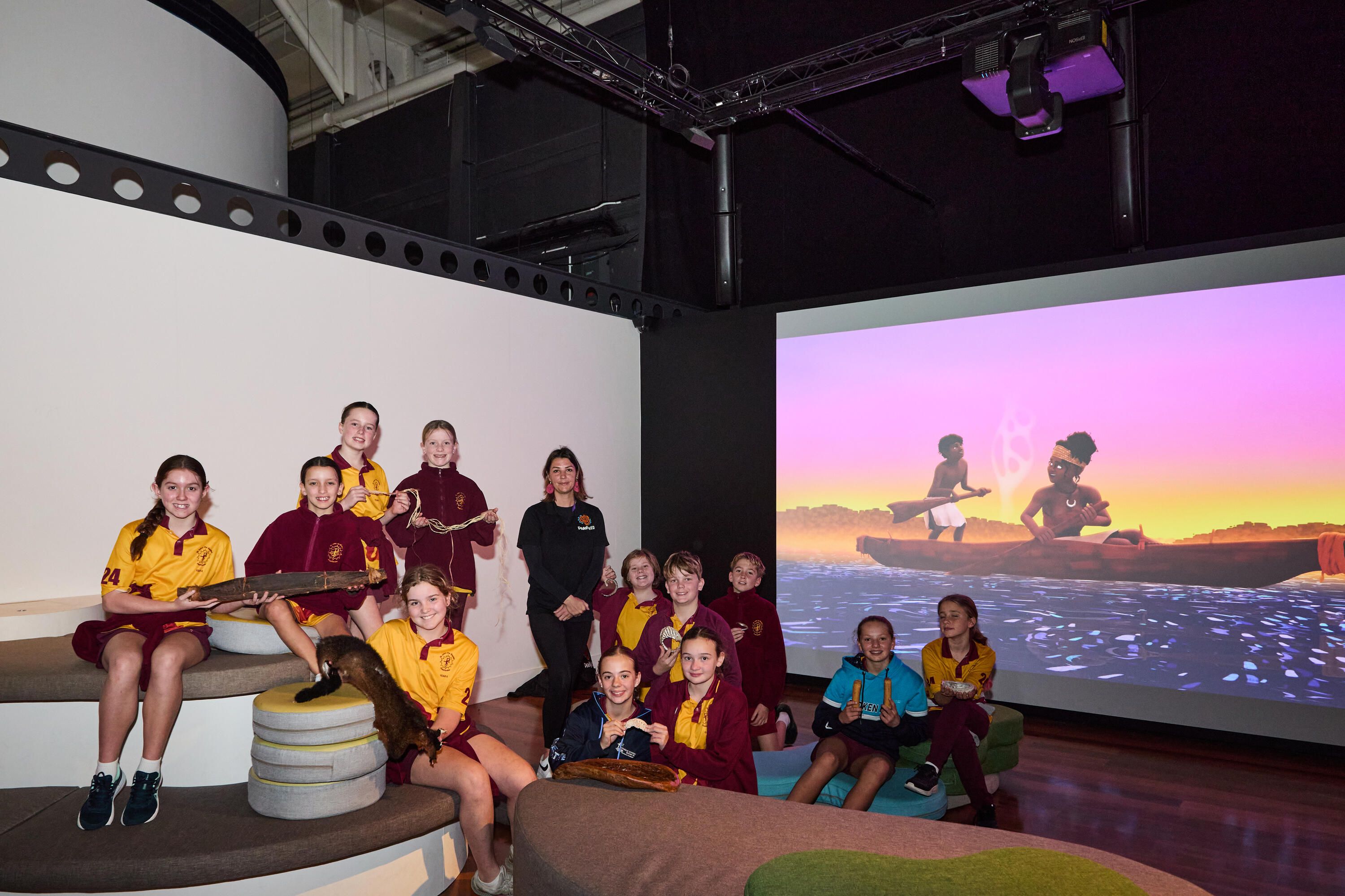 Group of students wearing school uniforms in a museum gallery space with a first nations woman in a black uniform.