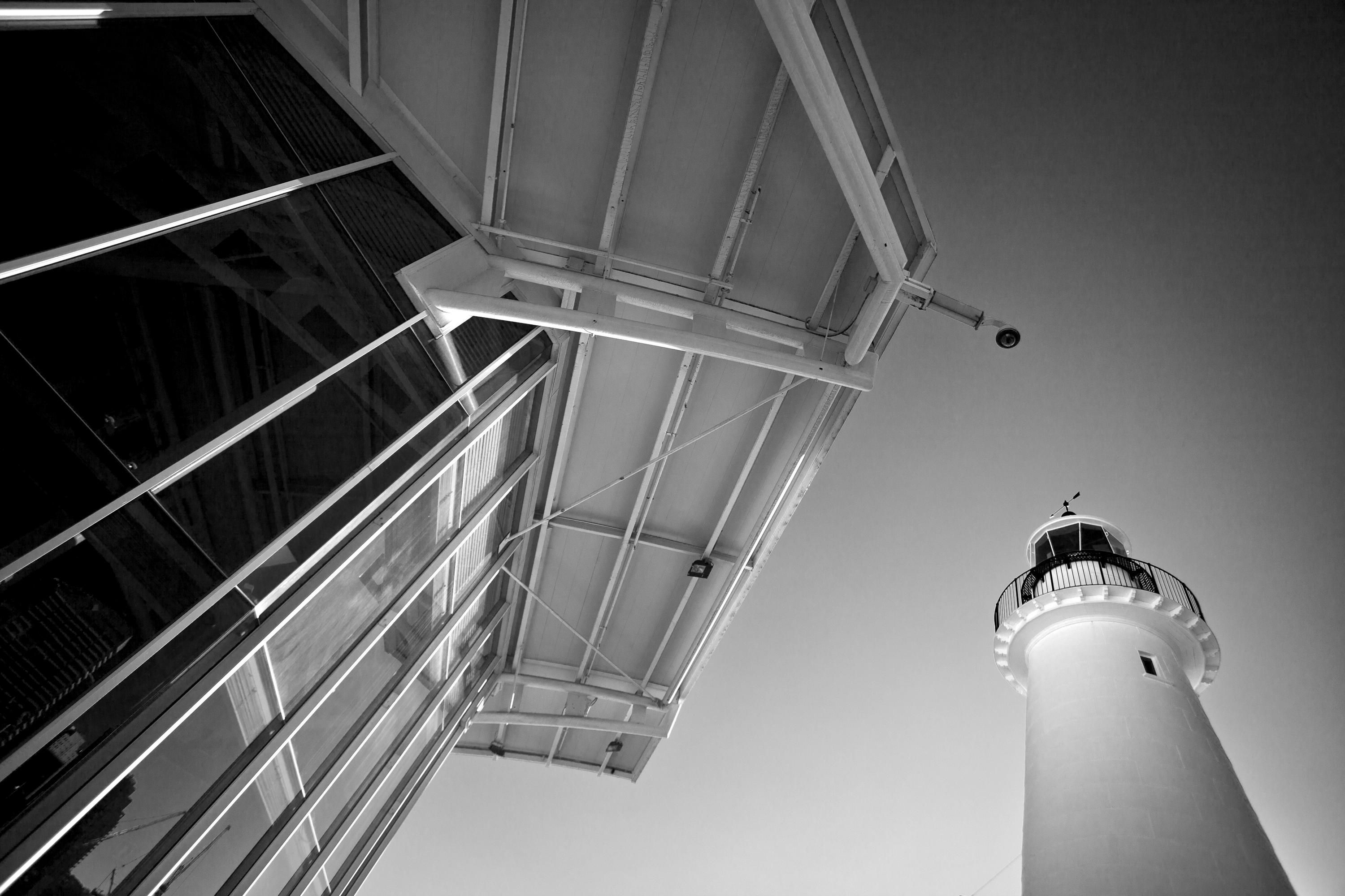 Black and white dramatic photo looking up at the edge of a modern building and a lighthouse. 