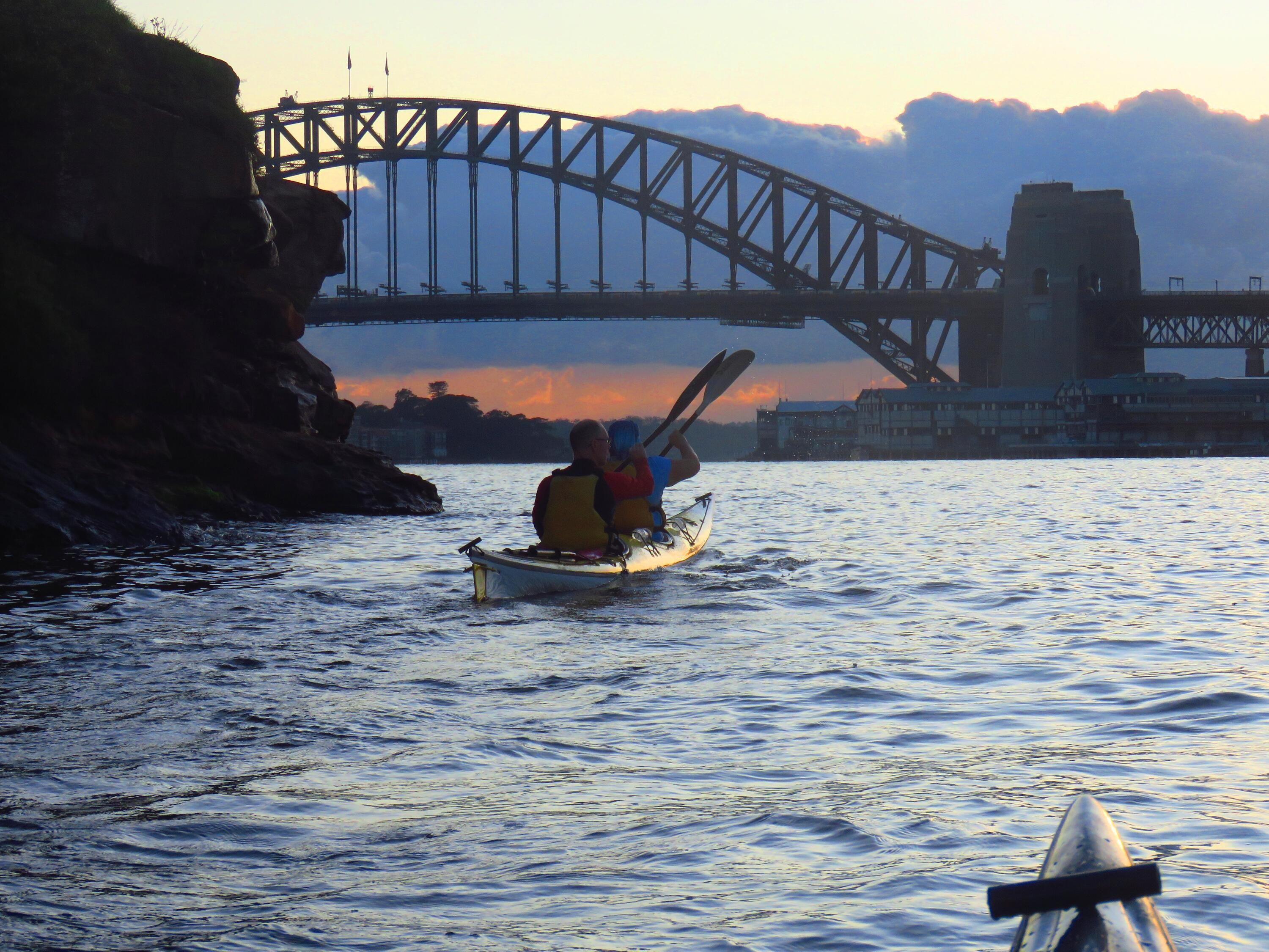 Photo taken from a kayack of another kayak paddling towards the harbour bridge. 