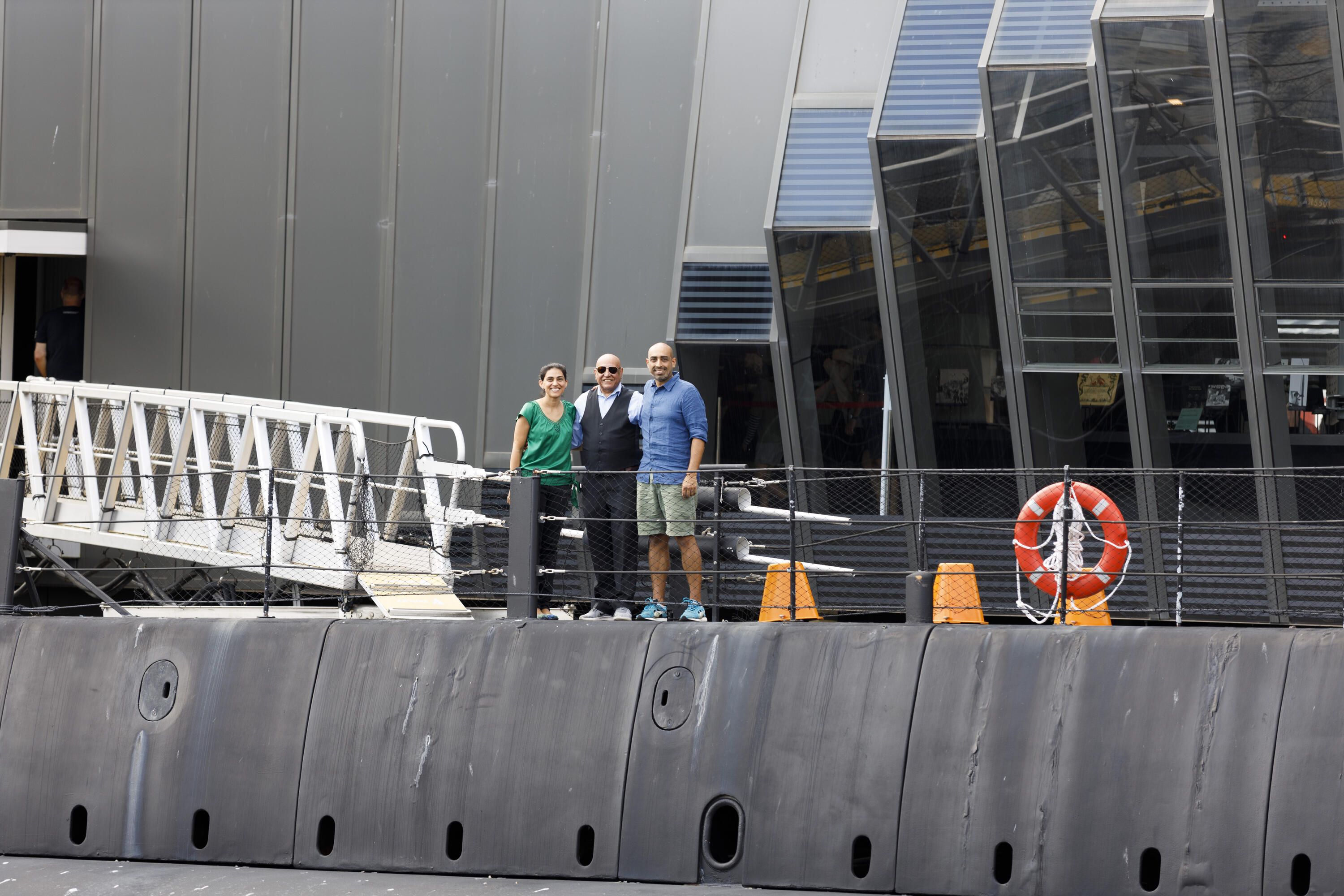 Photograph showing 3 people standing on the top of a black submarine.