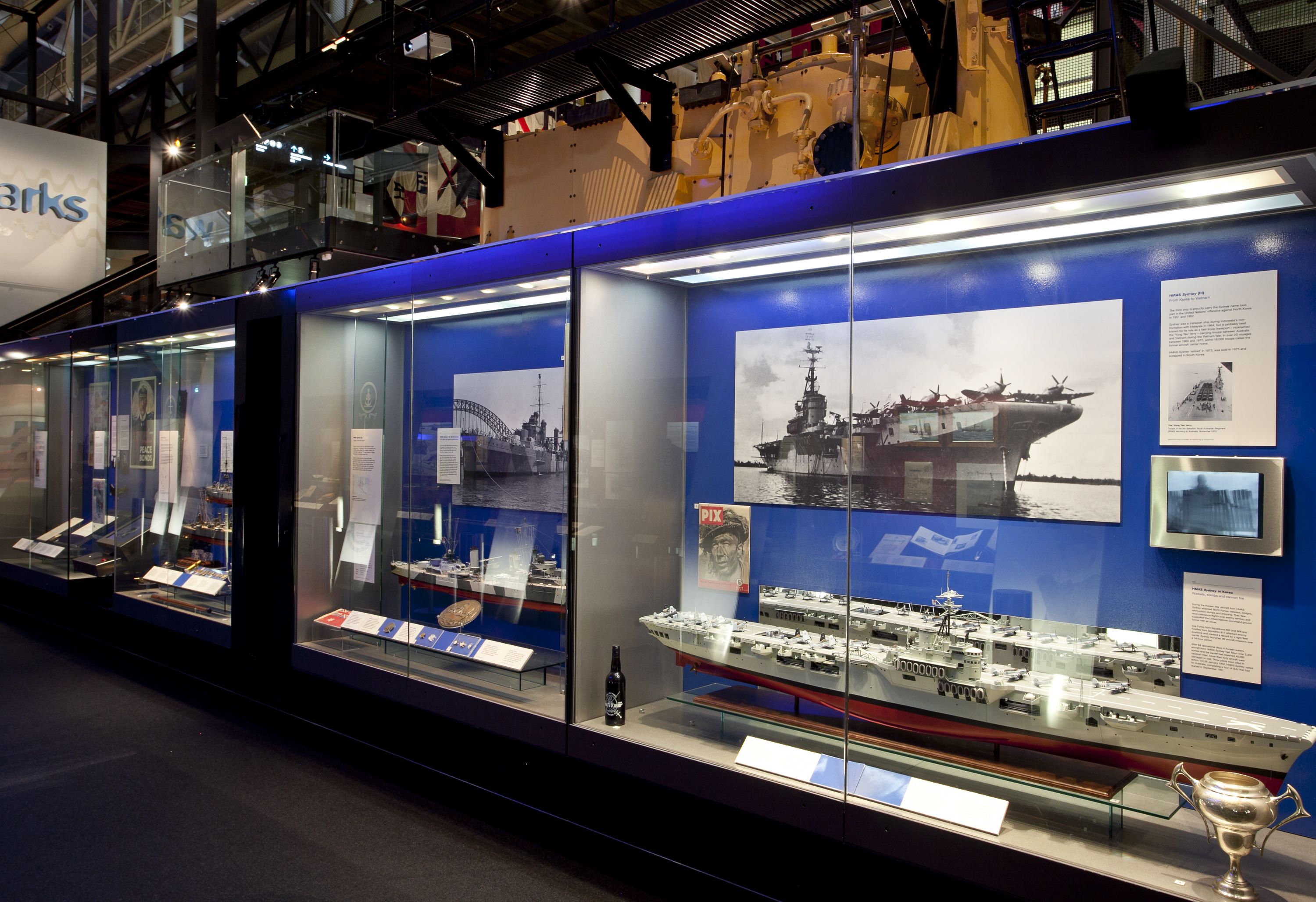 Photo showing a line of museum display cases containing ship models and photographs.