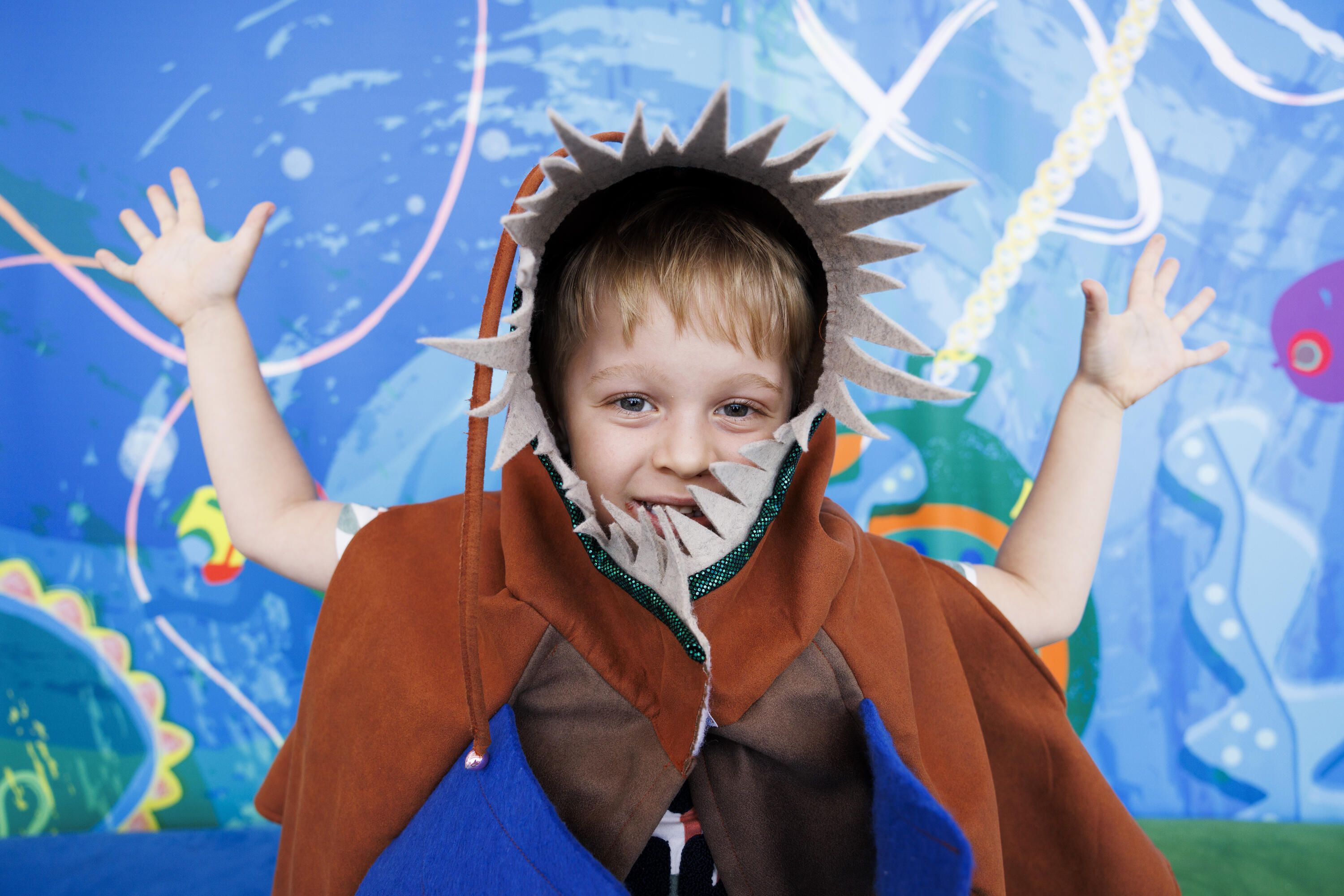 Pgotograph of a young boy wearing a dress-up featuring a hood with grey felt teeth.