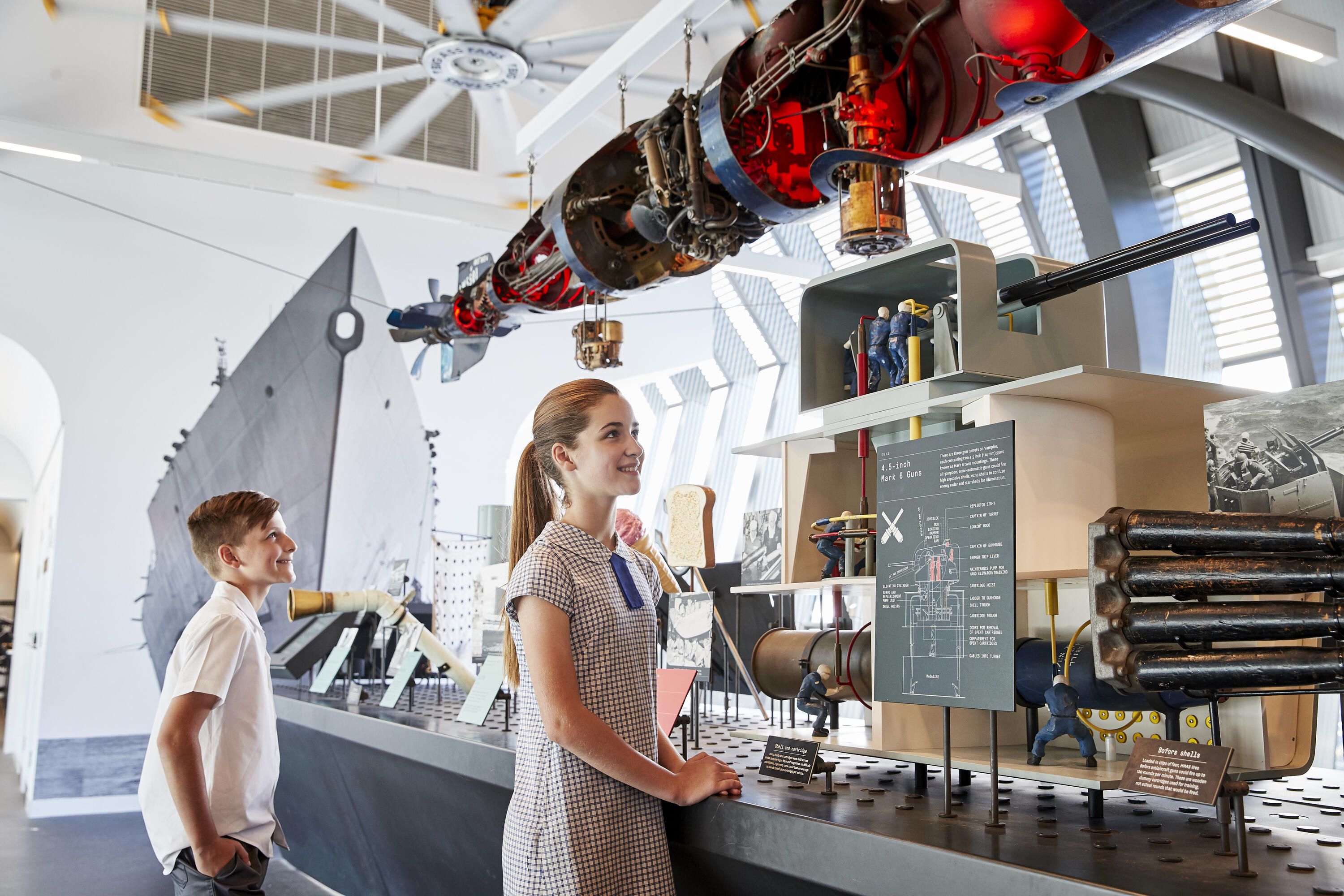 Photo of 2 children, a boy and a girl in a museum gallery looking at a Navy display. 