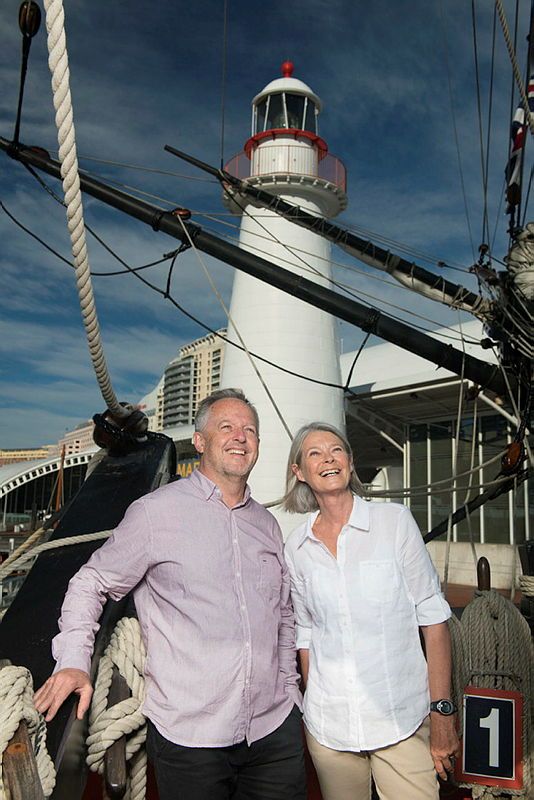 Photo showing an older couple standing on a ship with a lighthouse behind them