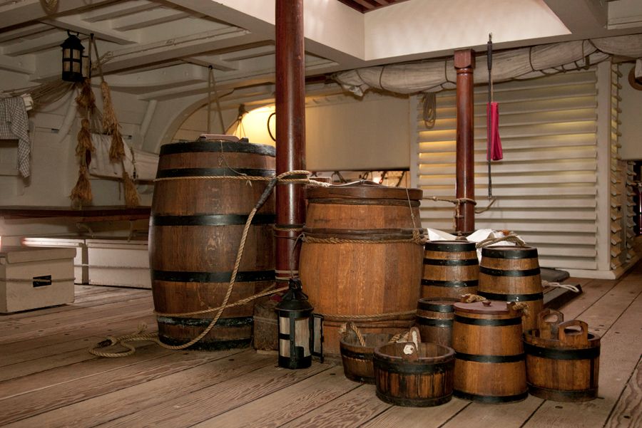 Photo showing a display of barrels and buckets below decks of a wooden tall ship.