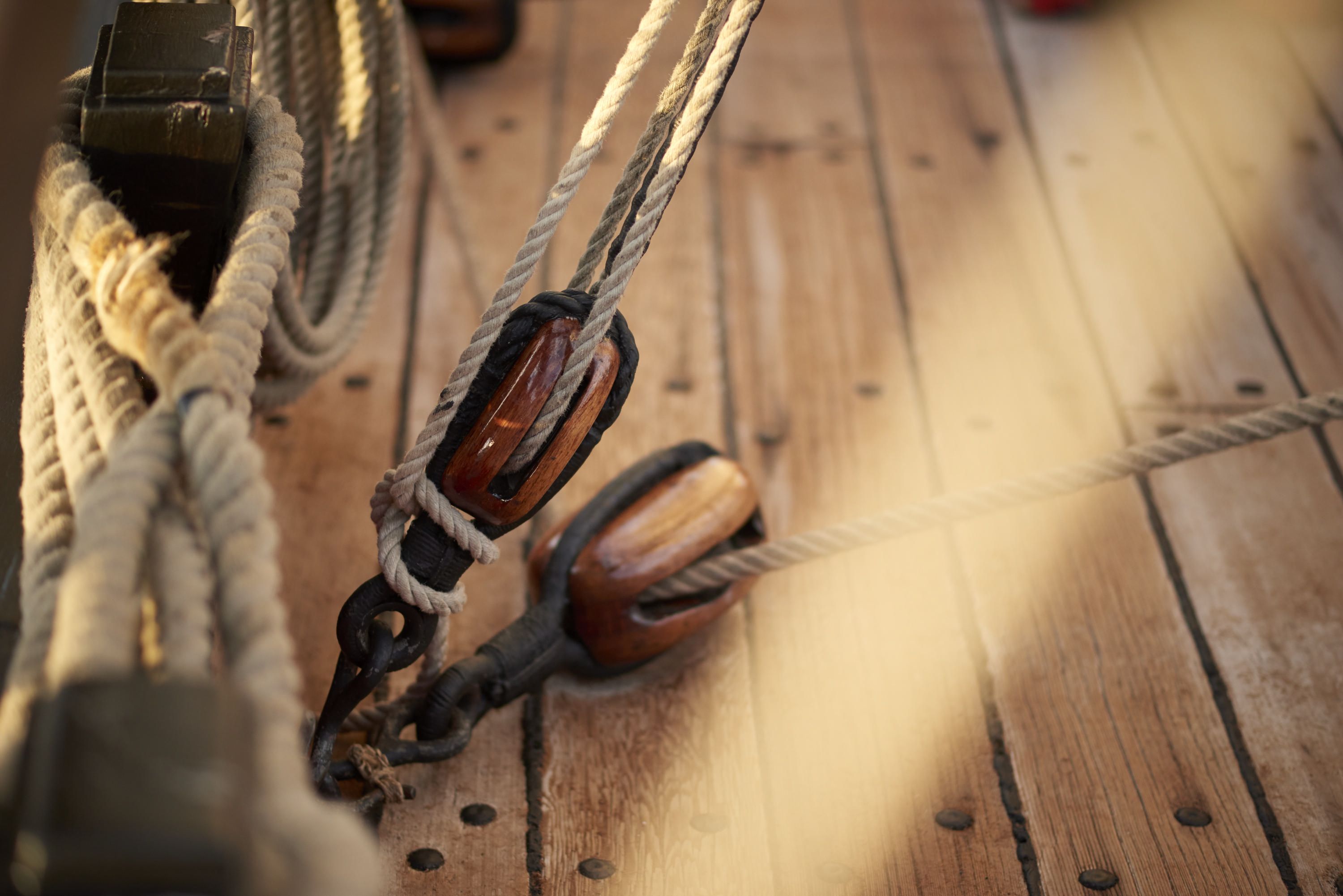 Close up photo showing ropes and pulleys on the wooden deck of a ship. 