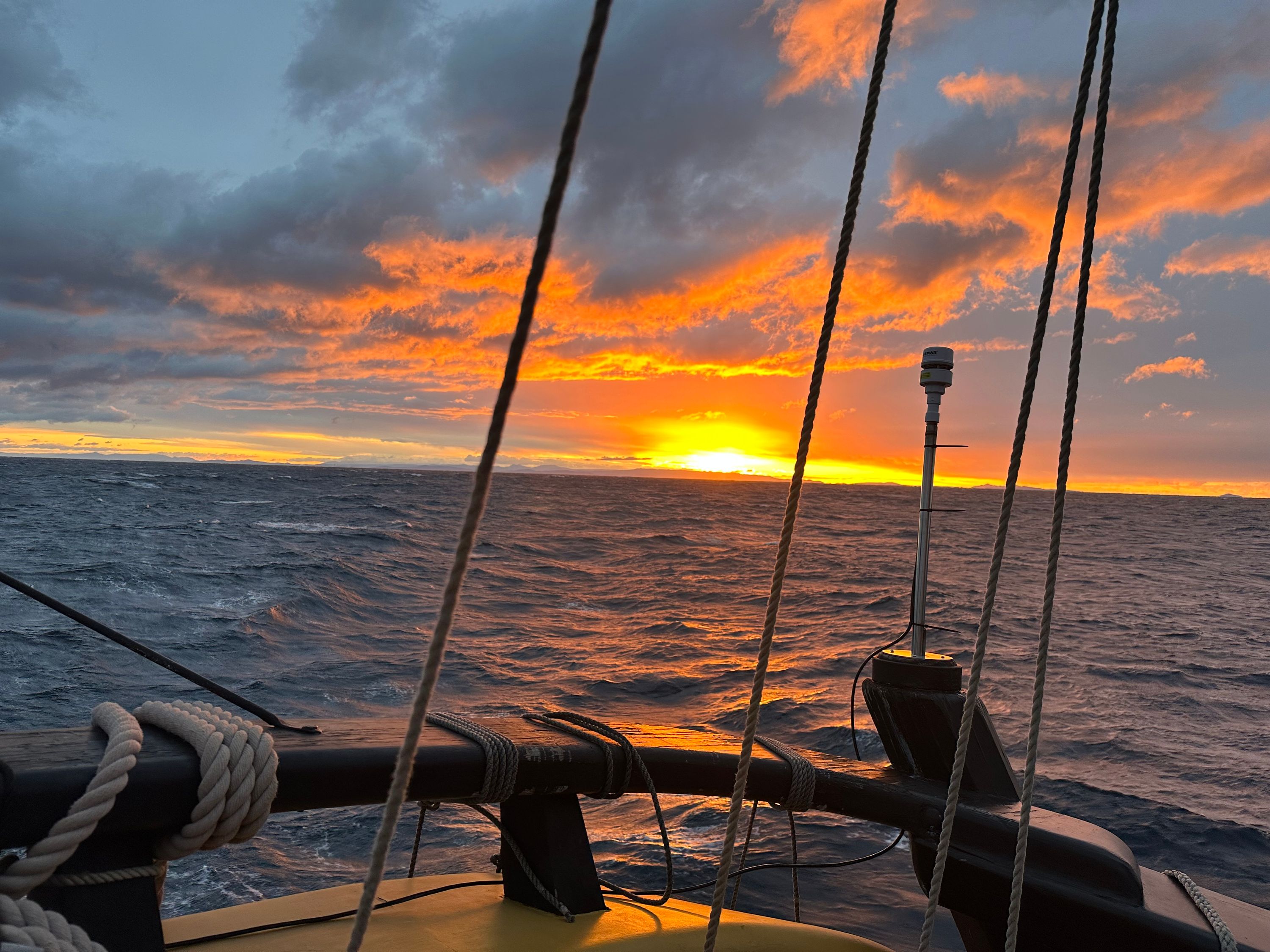 Photo of a sun on the horizon taken from the back of a tall ship.