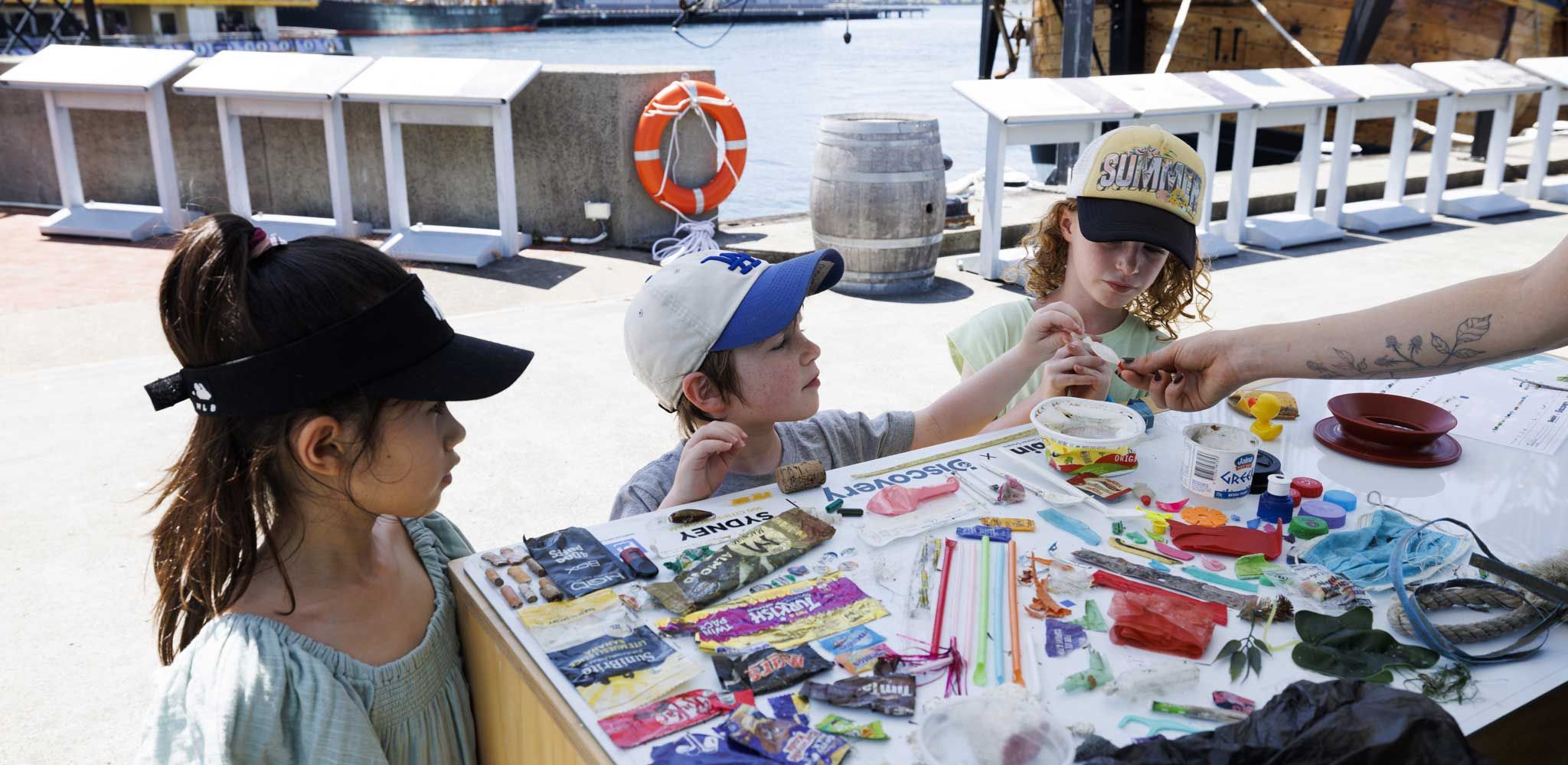 Photo of 3 children looking at a table covered with examples of rubbish