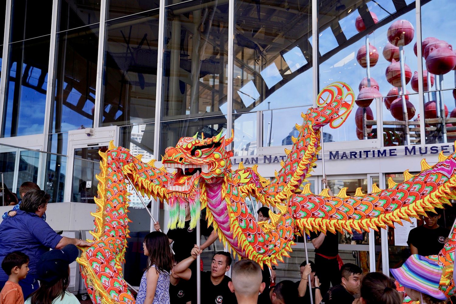 Photo showing a large dragon puppet controlled my multiple people with sticks holding it above their heads..