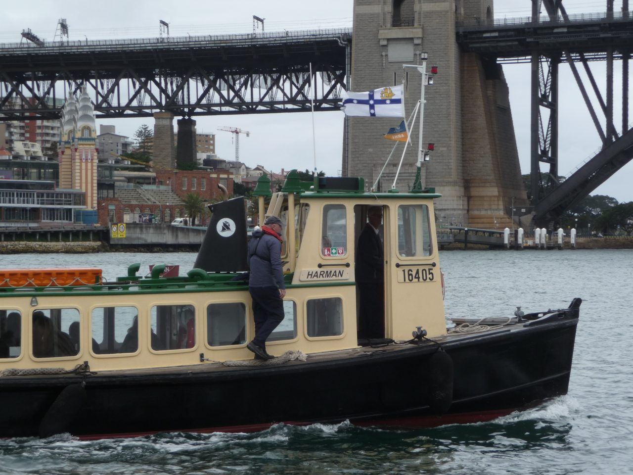 Photo showing a small yellow and black boat with green trim. Part of the Sydney harbour bridge can be seen in the background.