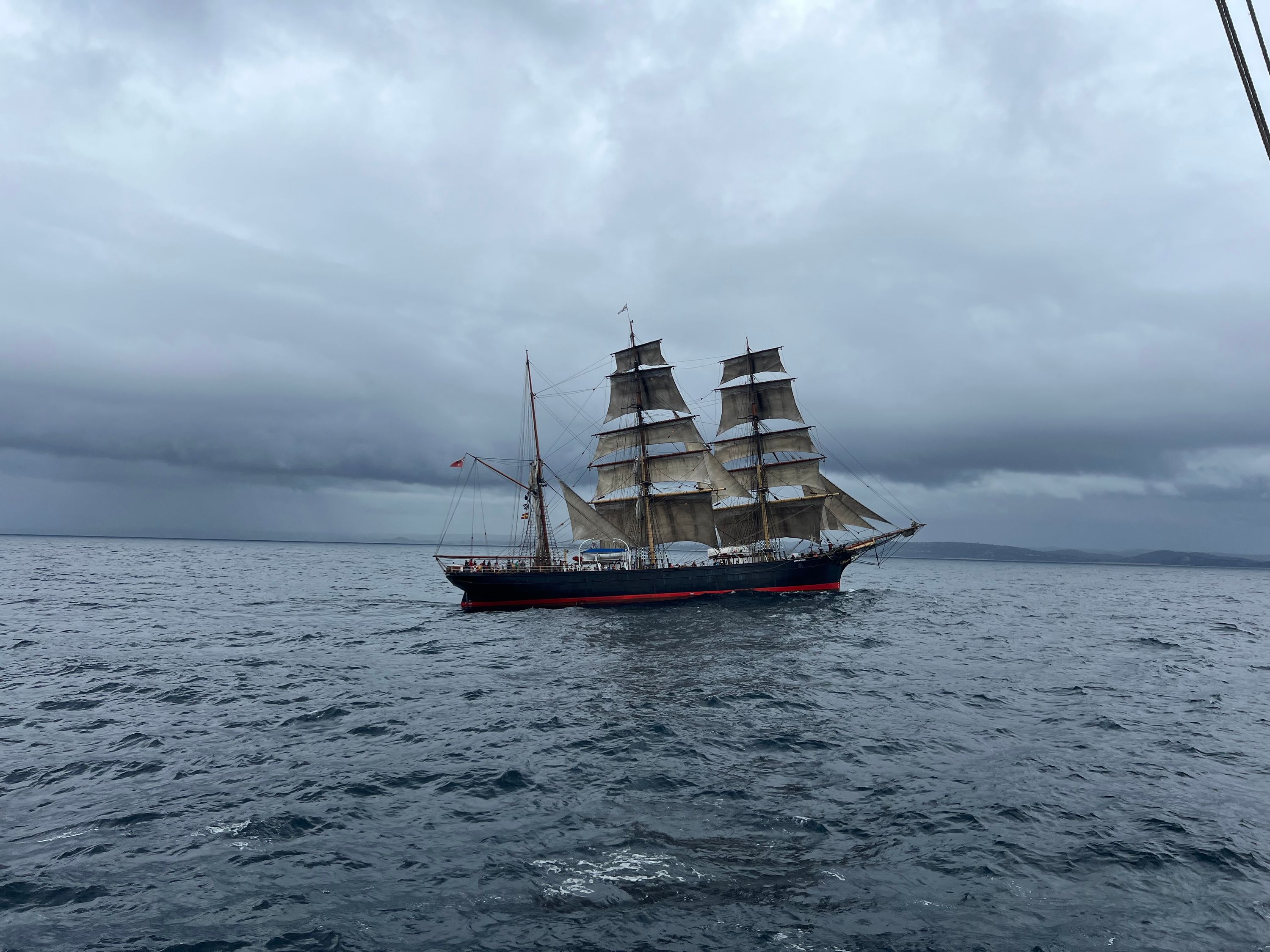 Photo of a tall ship with a black hull and sails up.