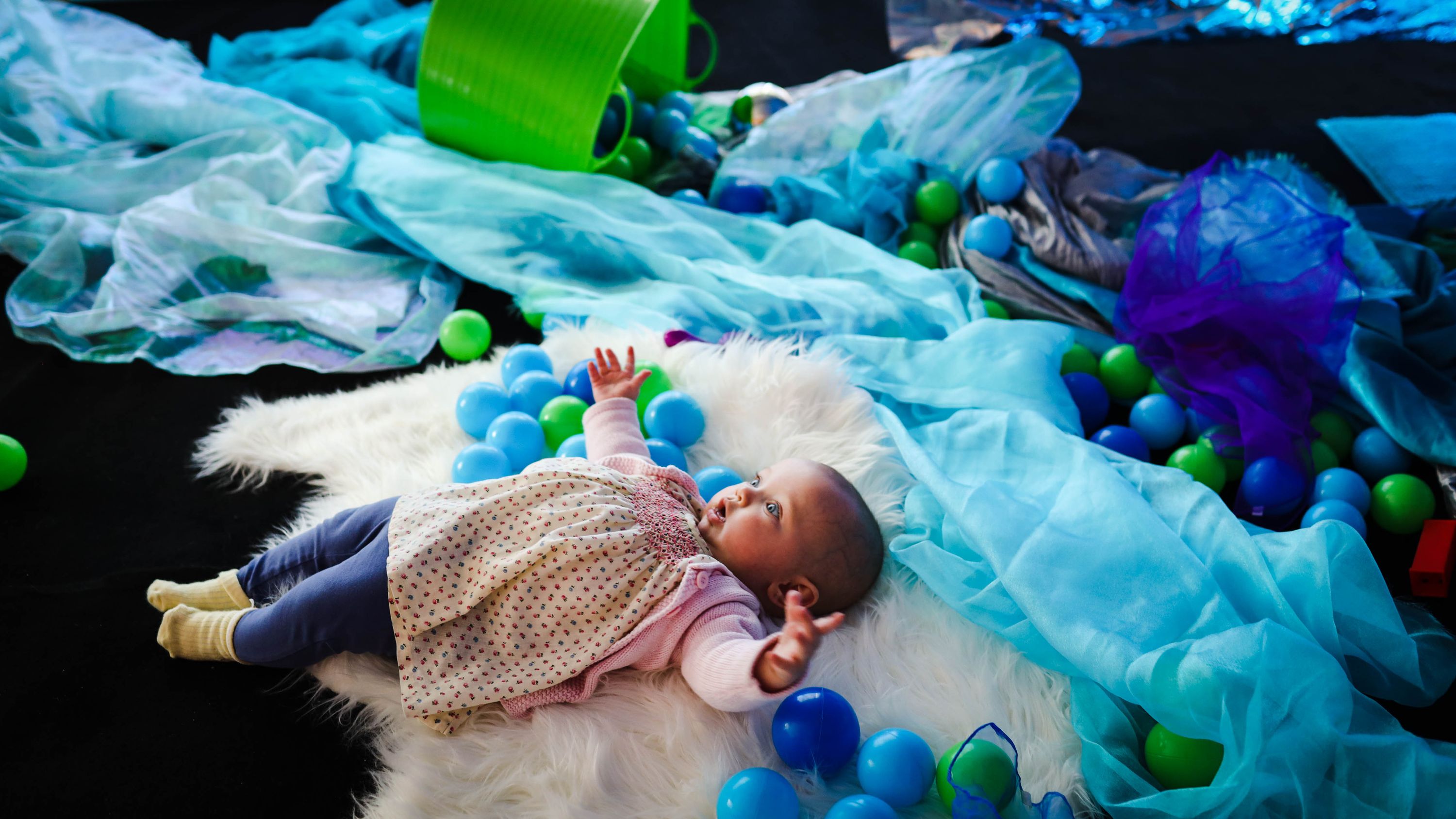 A baby in the play space surrounded by balls.