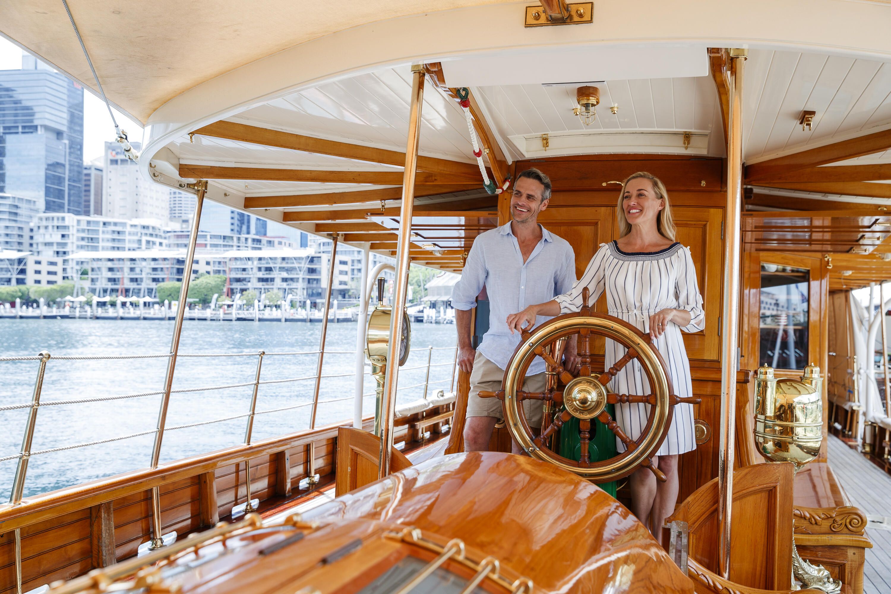 A couple aboard the Edwardian steam yacht SY ENA, posed behind the ship's wheel.
