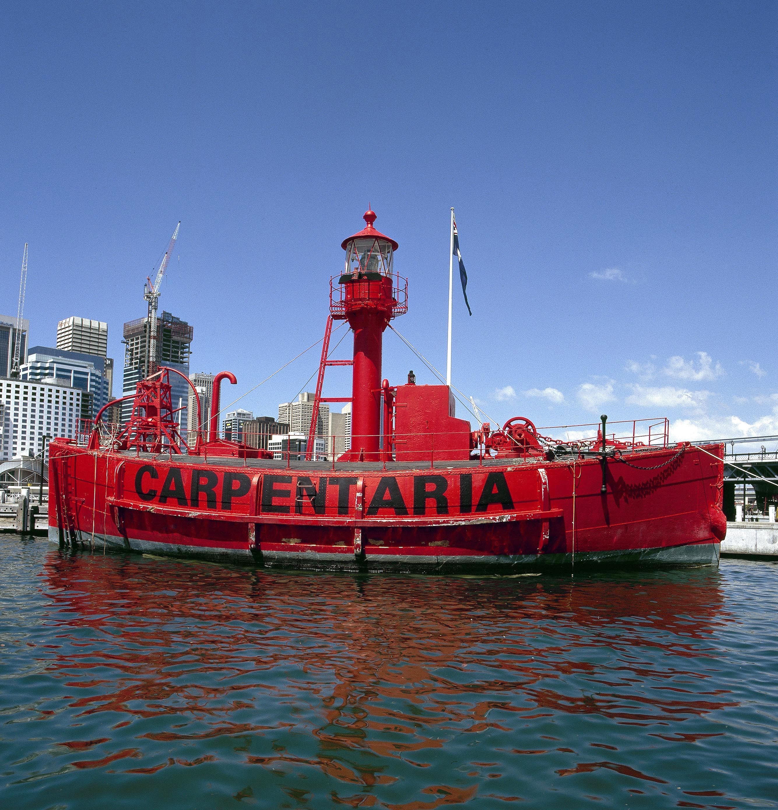 Photograph of a red lighthouse ship, with the name CARPENTARIA in black along the side on the water.