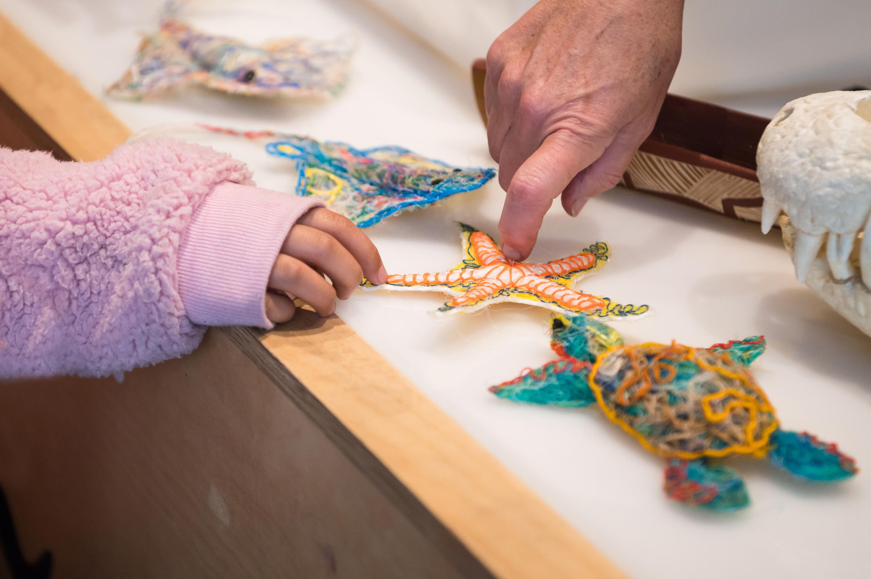 Photo showing hands touching small sculptures in the shapes of sea creatures, made from recycled fishing line.