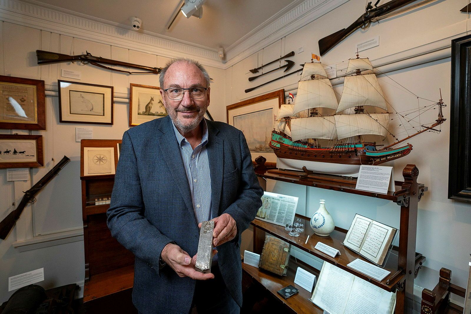 Photo of a man holding a metal object. He is standing in a museum gallery.