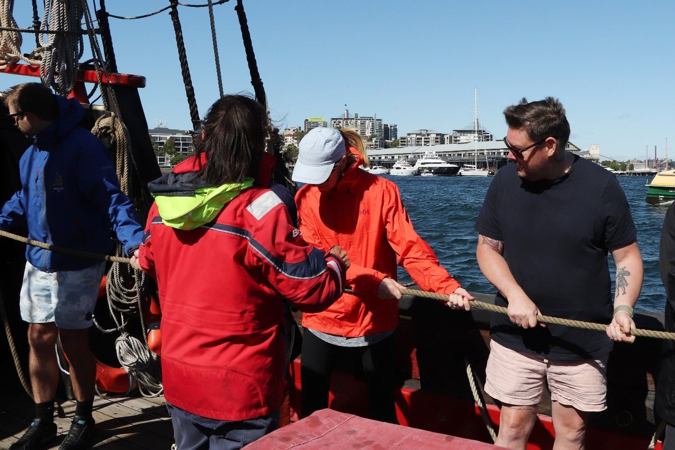 Photo showing people pulling a rope on a ship, with the harbour in the background.