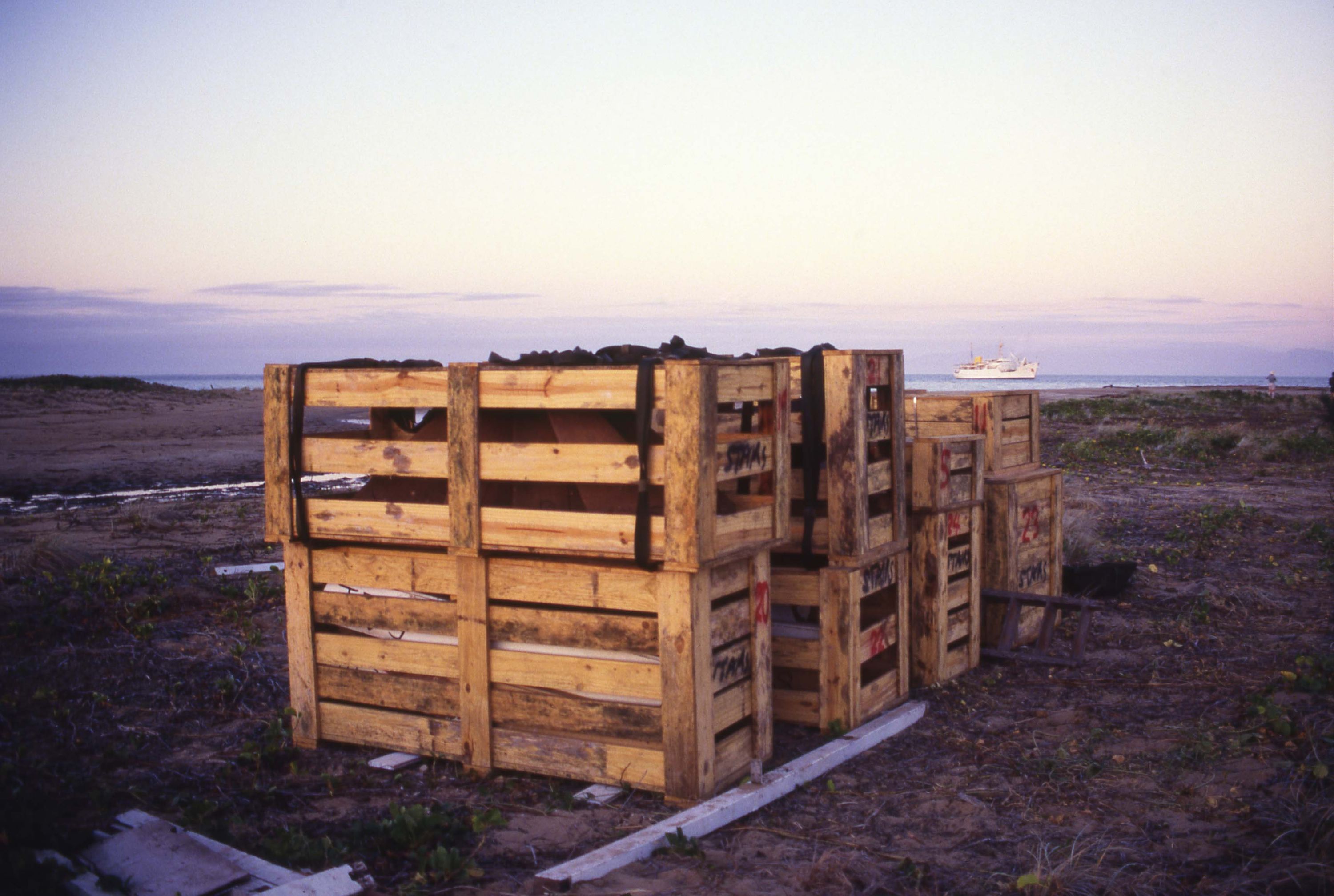 Photo showing wooden crates stacked up on a beach.