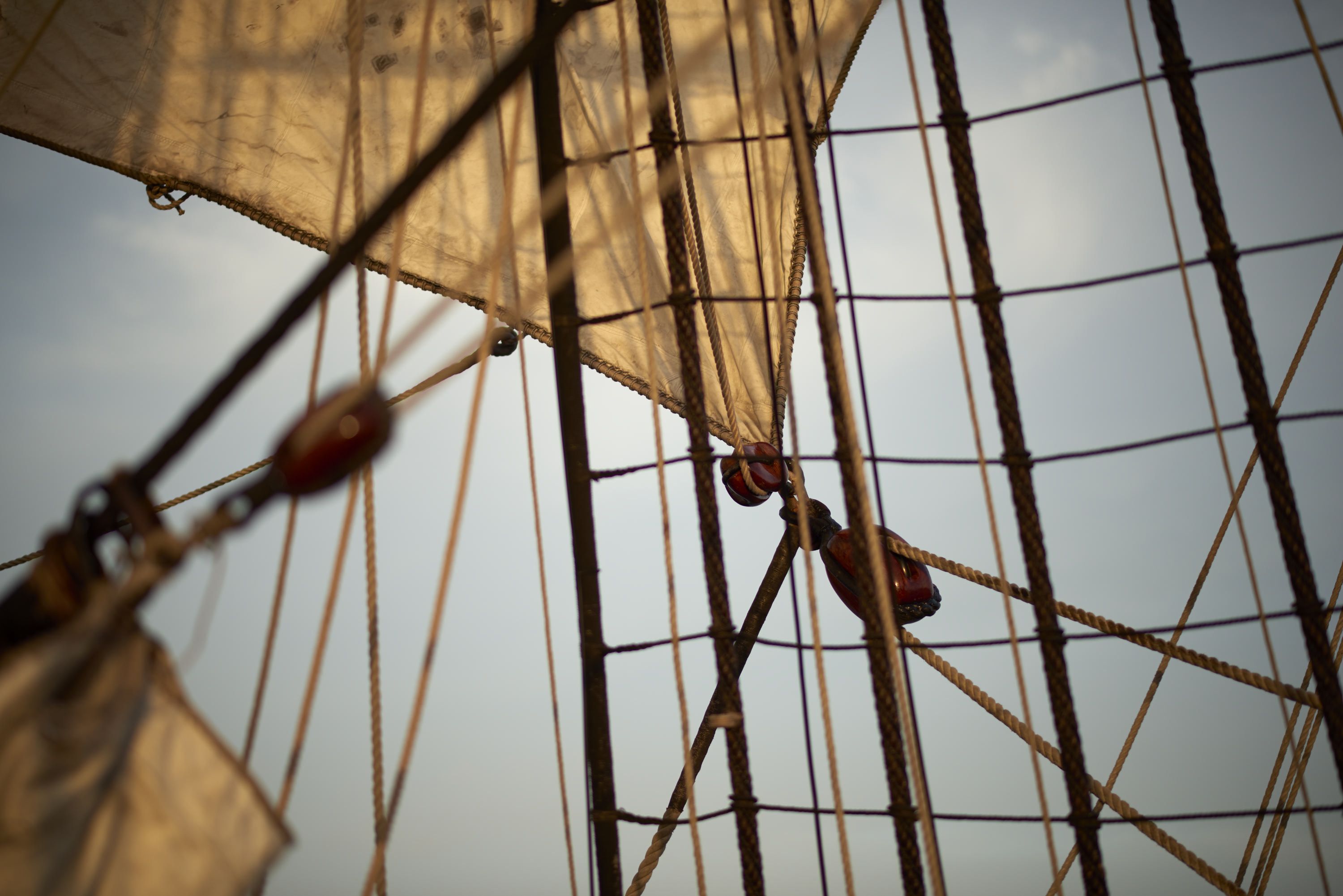 Photos of ropes, pulleys, rigging and sails, with a grey sky behind. 