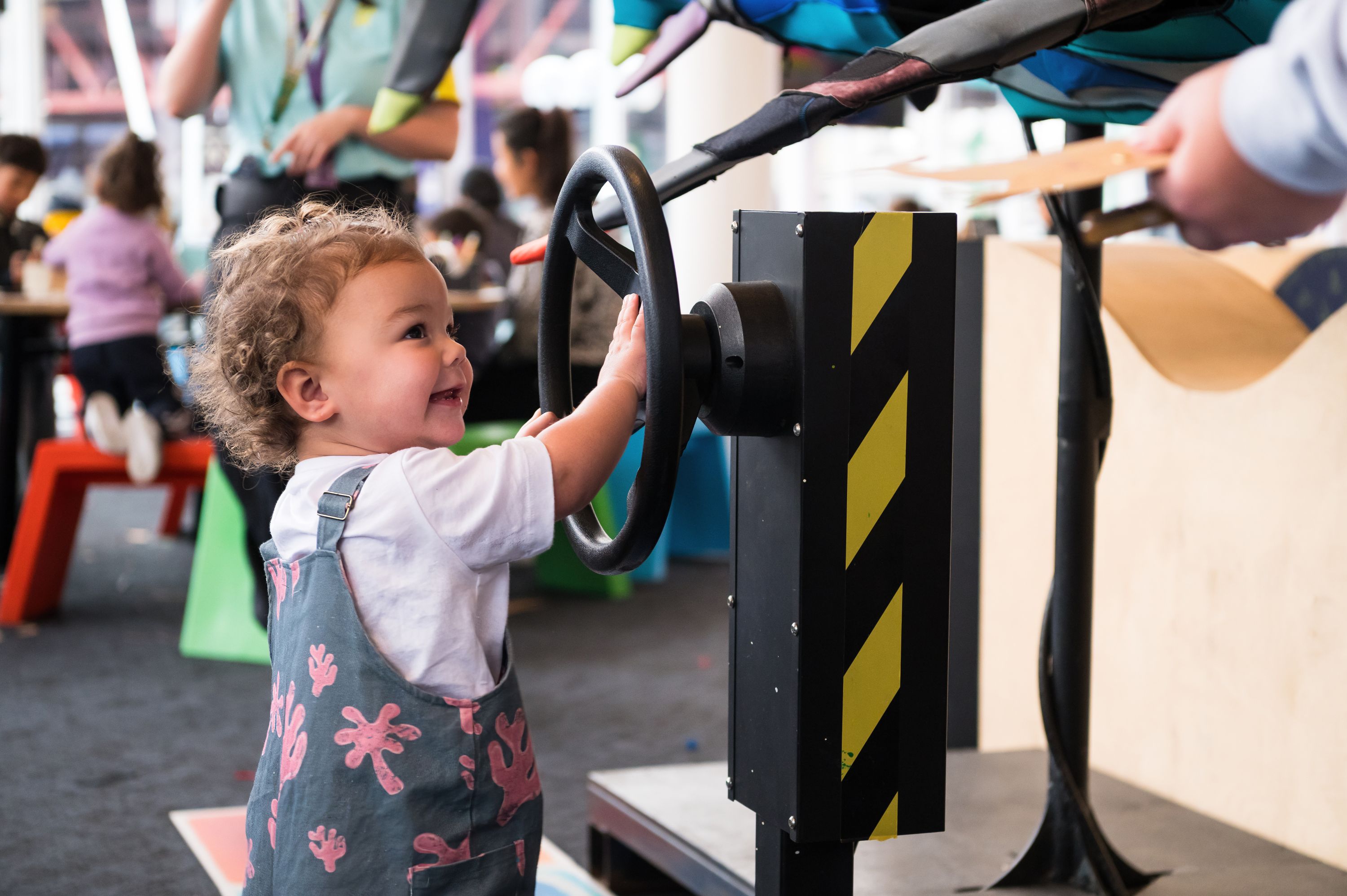 Photo of a toddler smiling while playing with a steering wheel interactive