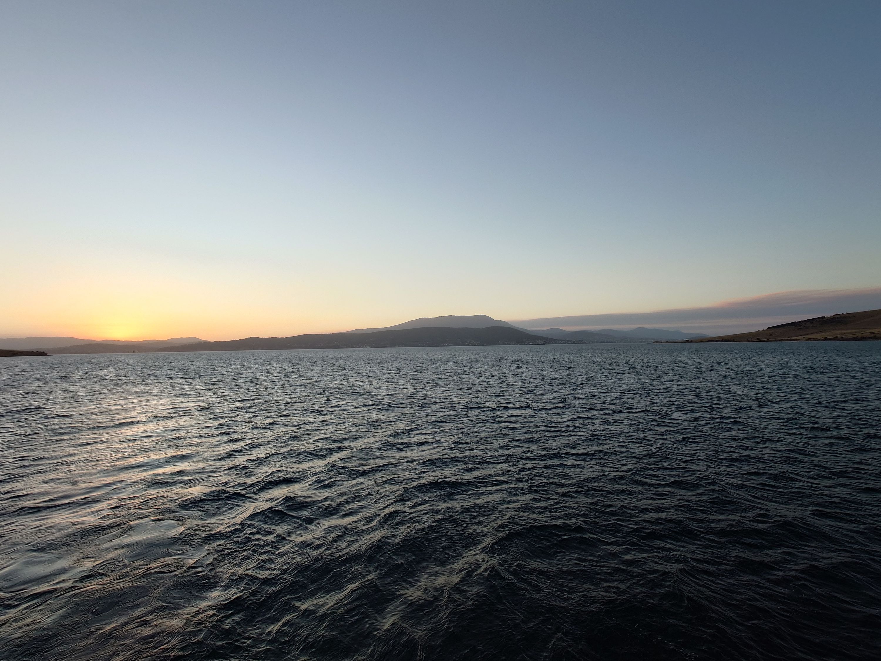 Photo taken from a boat at sunset, with land in the distance. 