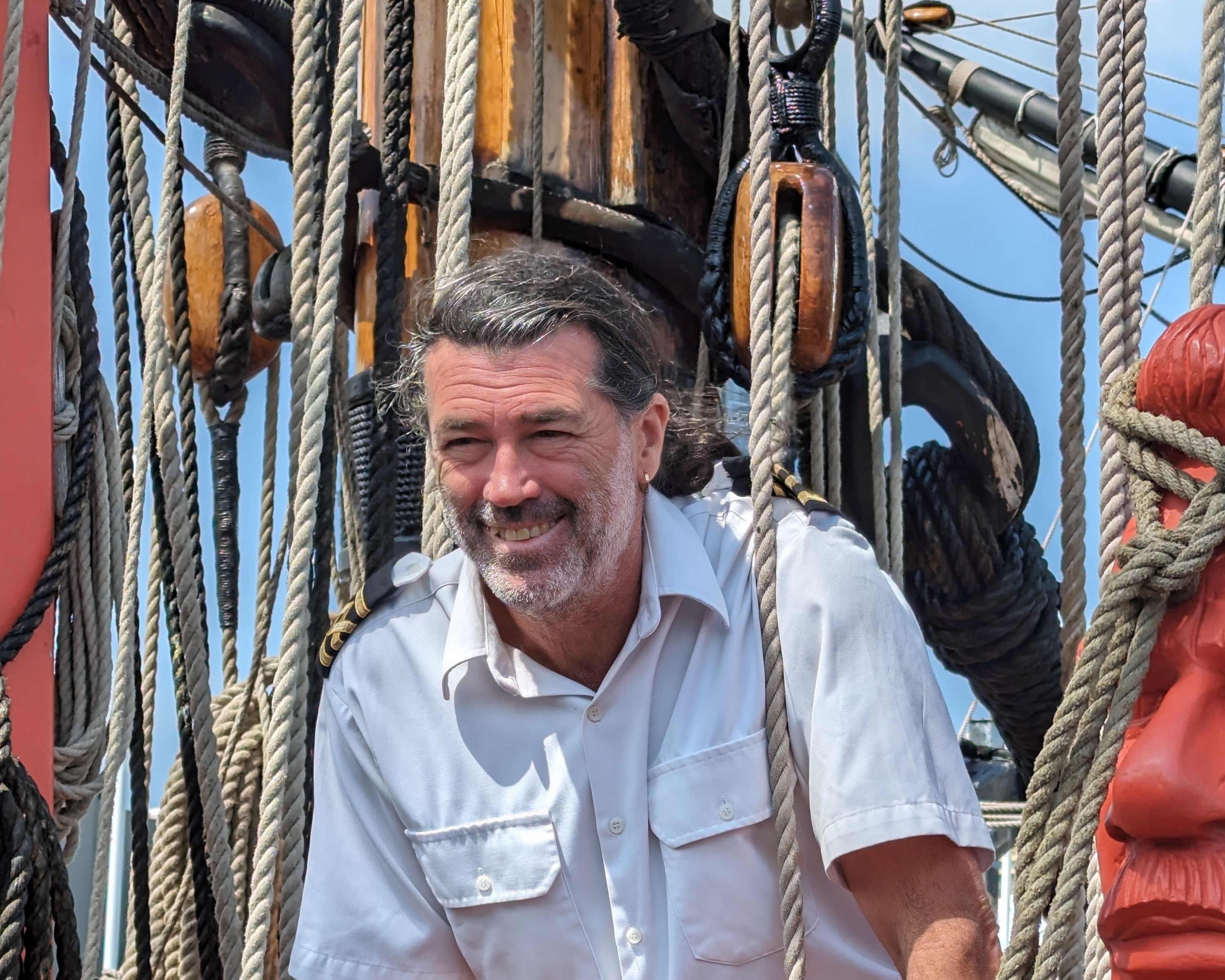photo of captain of endeavour standing and smiling, with the mast and ropes behind him.