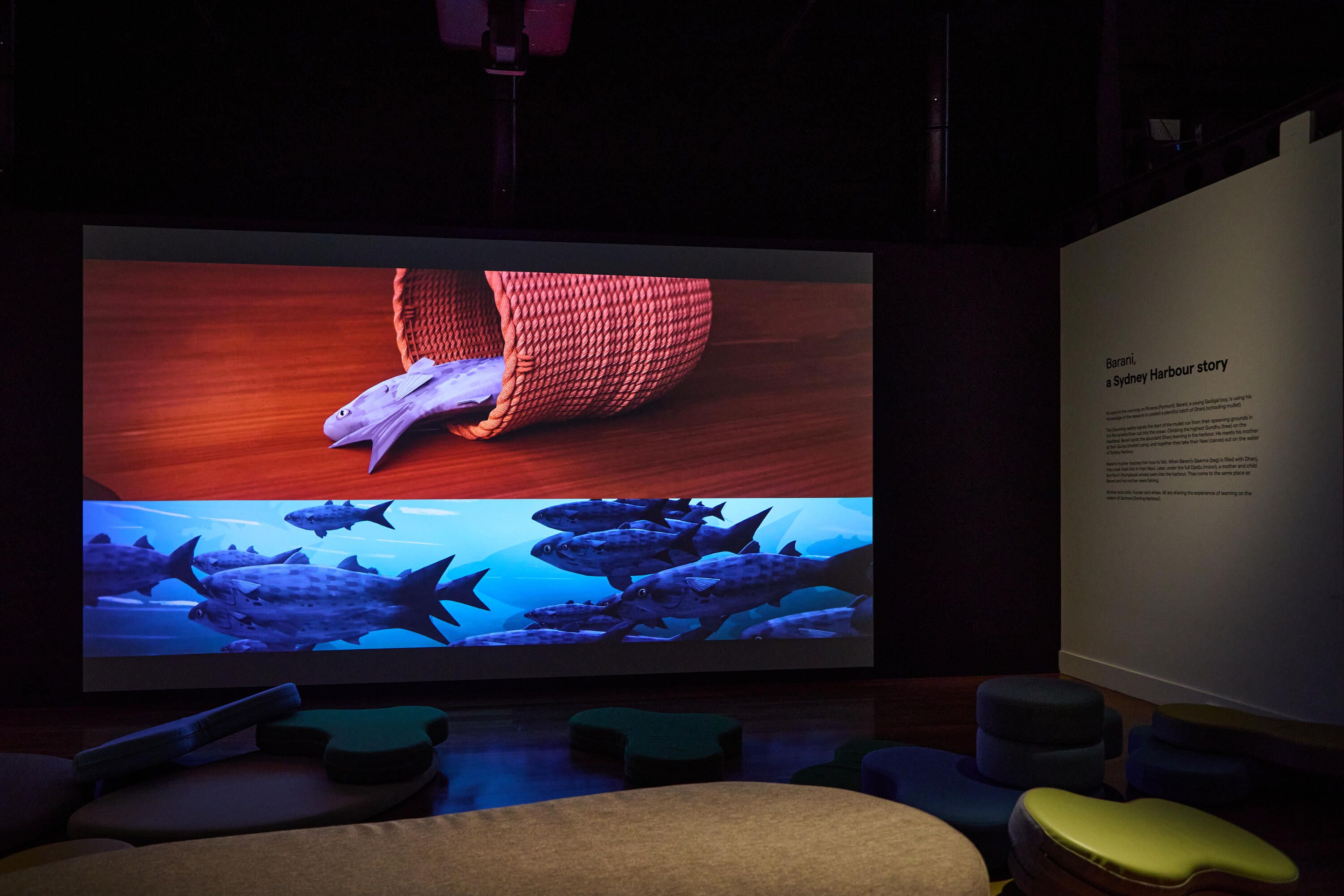 Photo of a museum exhibition space with curved soft seating and a large projection screen