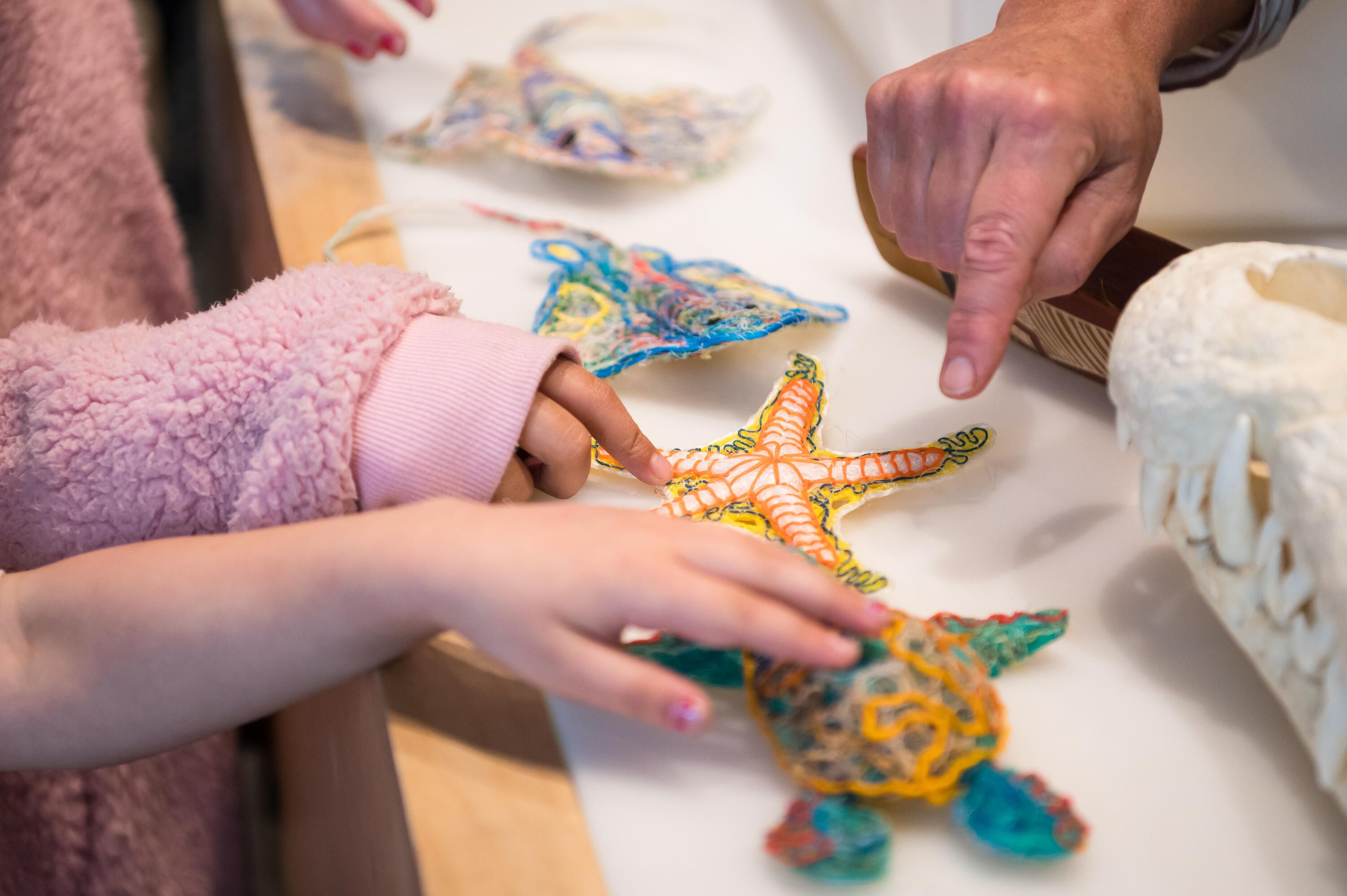 Photo showing hands touching small sculptures in the shapes of sea creatures, made from recycled fishing line.