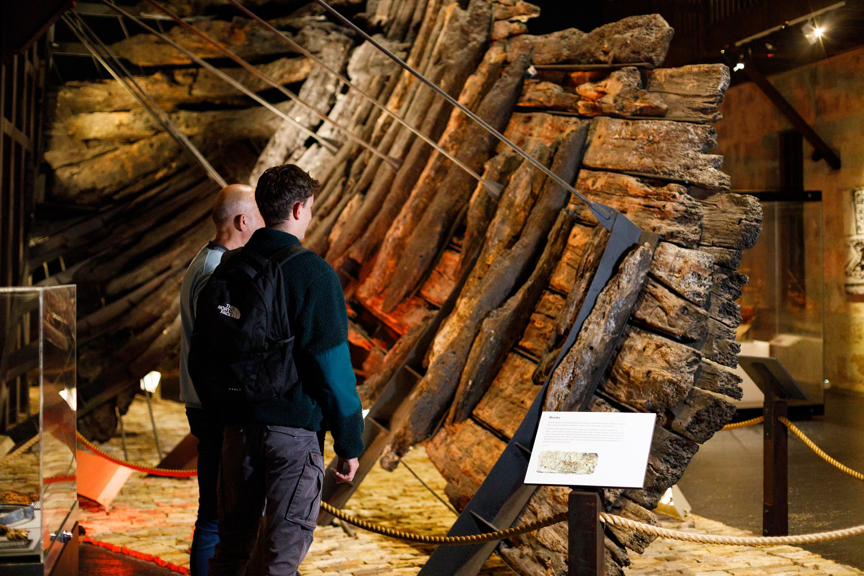 Photo of 2 people looking at a museum display of a shipwreck.