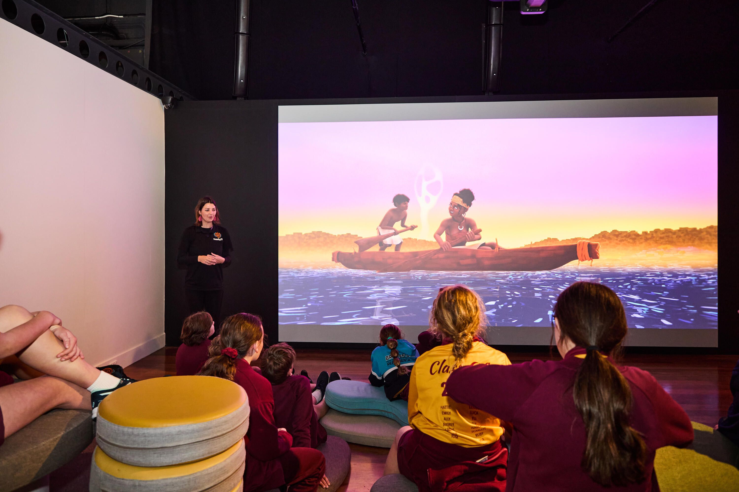 Photo of students in a museum exhibition space with curved soft seating and a large projection screen