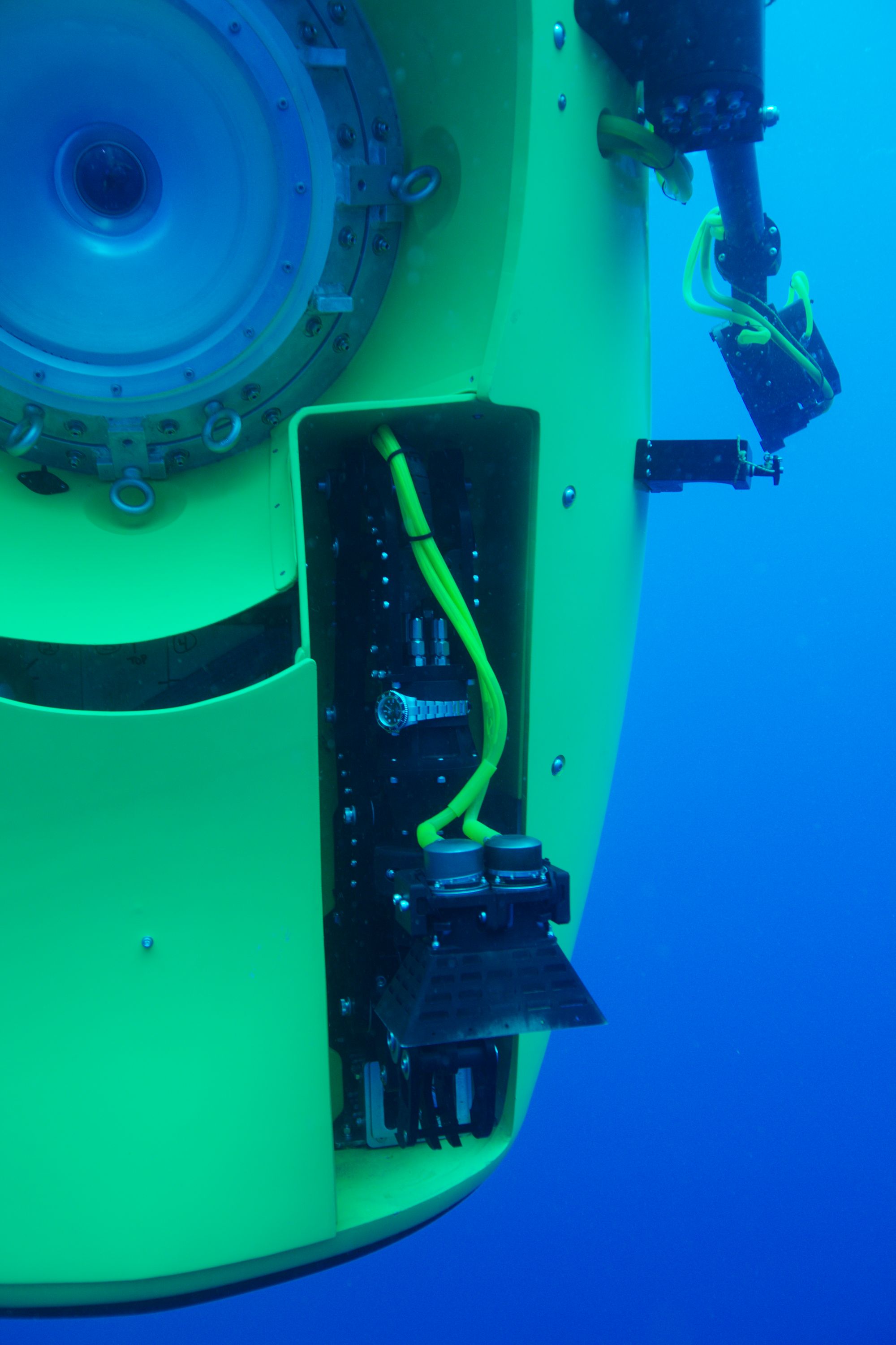 Photo taken underwater showing a close up of the outside of a submarine with a silver watch attached.