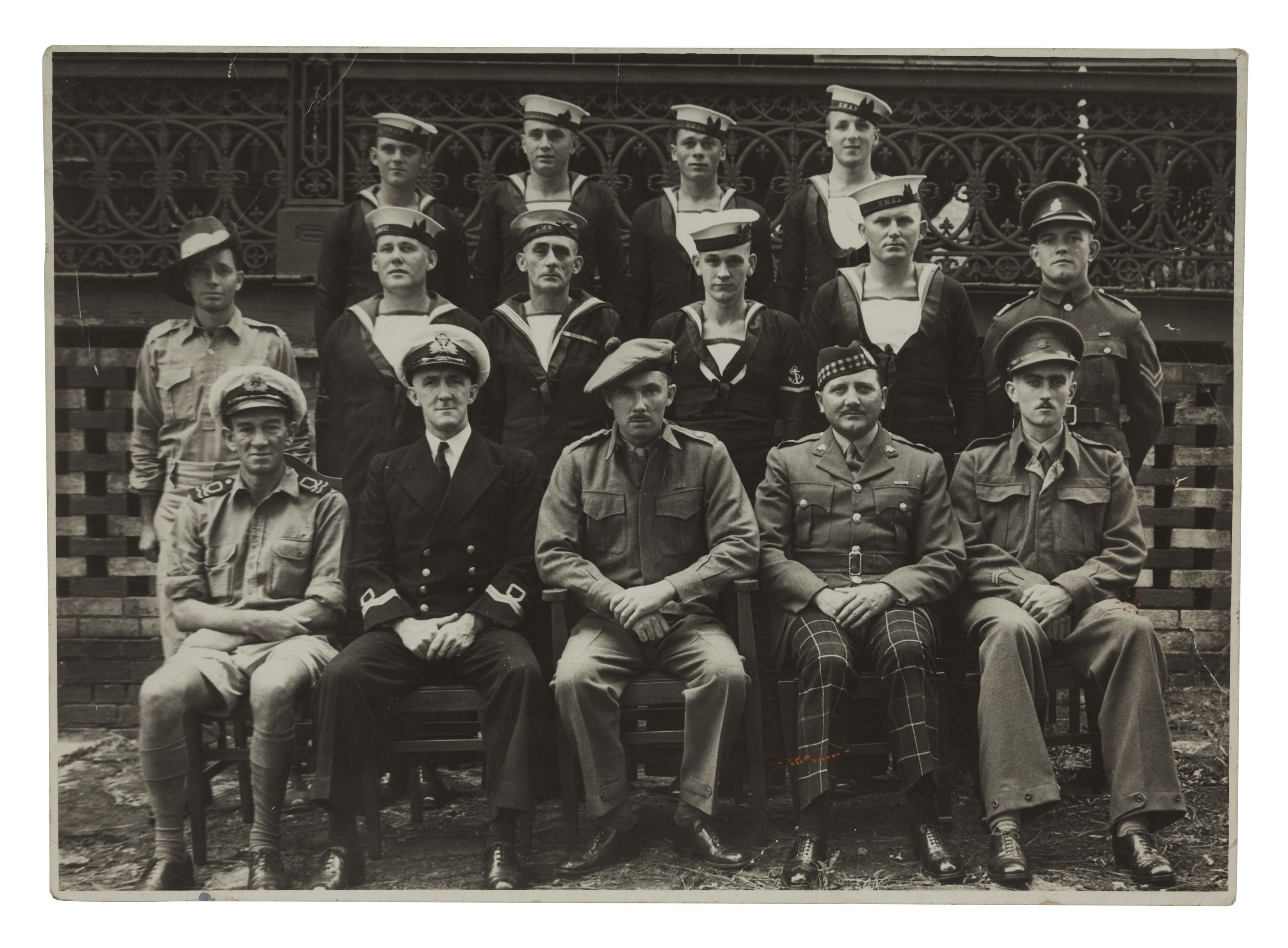  The photo pictures a group of 15 men seating in three rows. The men are wearing navy uniforms