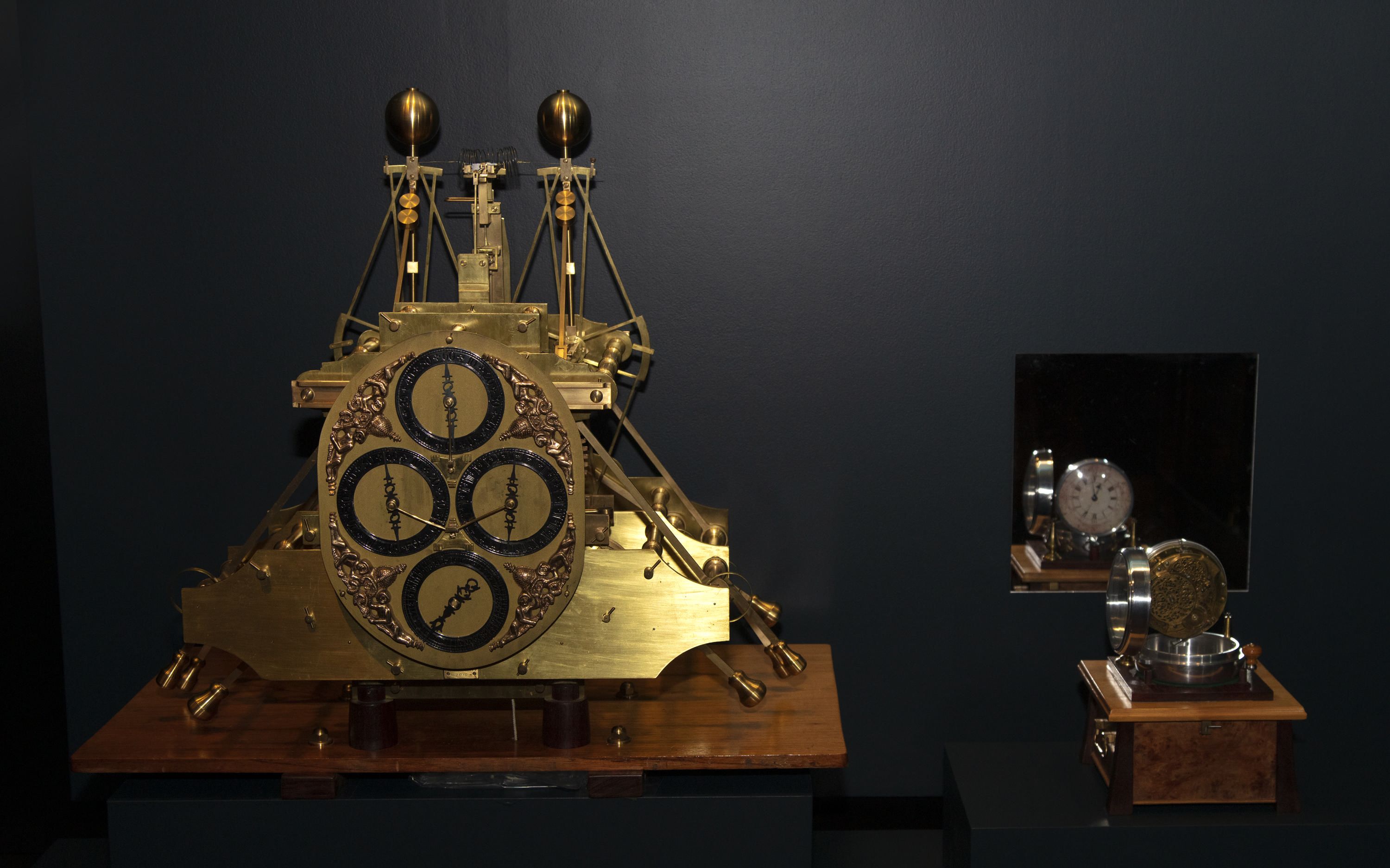 Photograph of a museum display case containing a large and small antique clock model. 