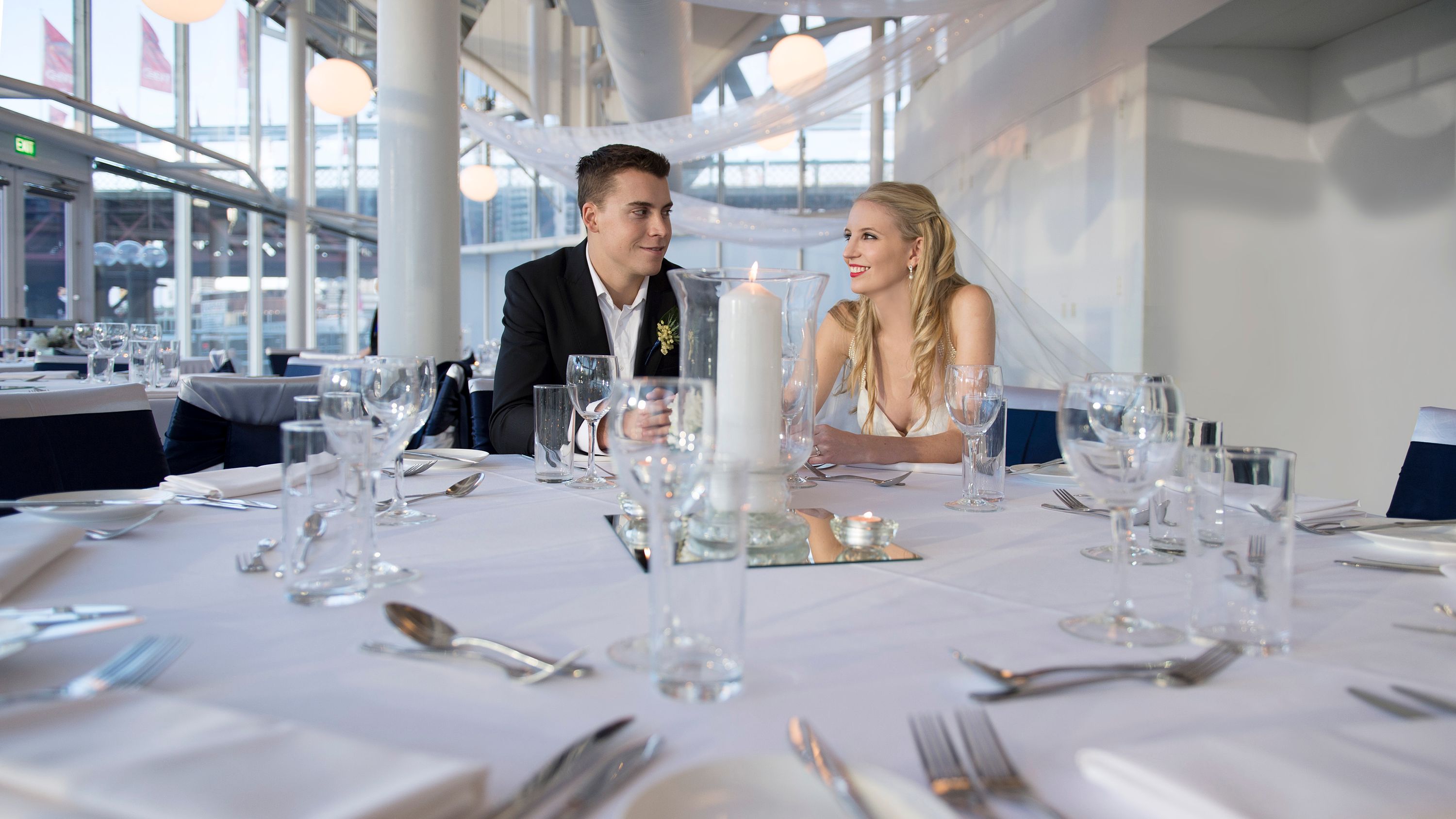 a bride and groom sitting at a large round table set up for a wedding reception