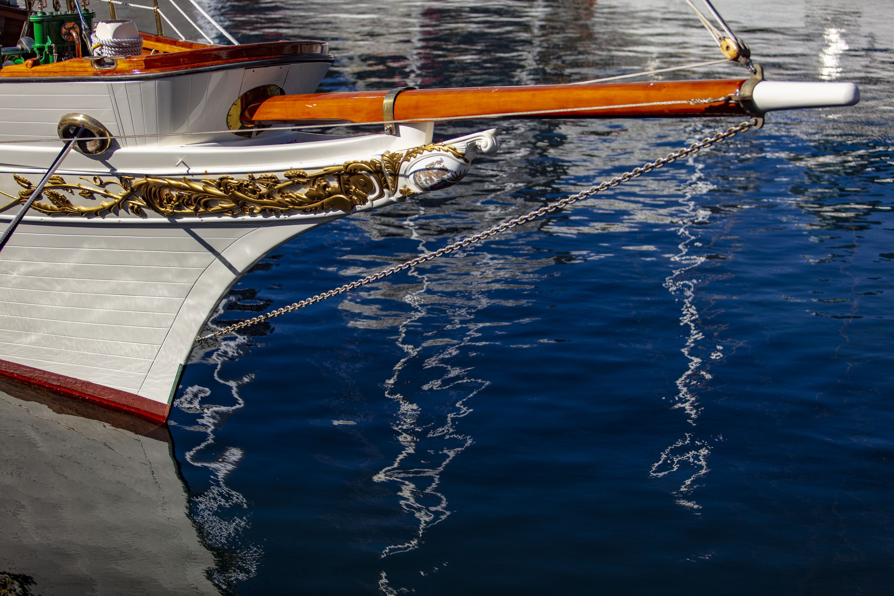 Photo showing the bow, front, of a wooden boat with a white painted hull and gold details. 