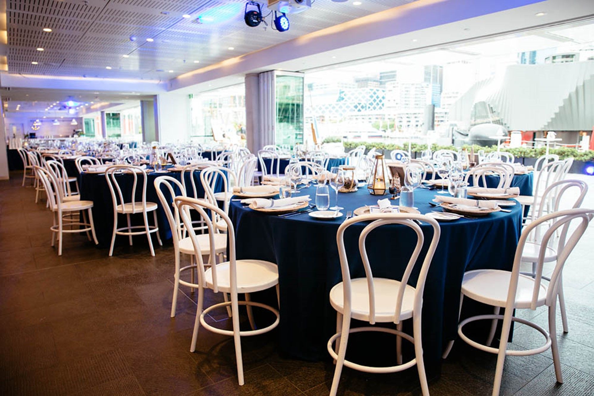 photo of event space with white chairs and large round tables with dark table cloths and place settings. 