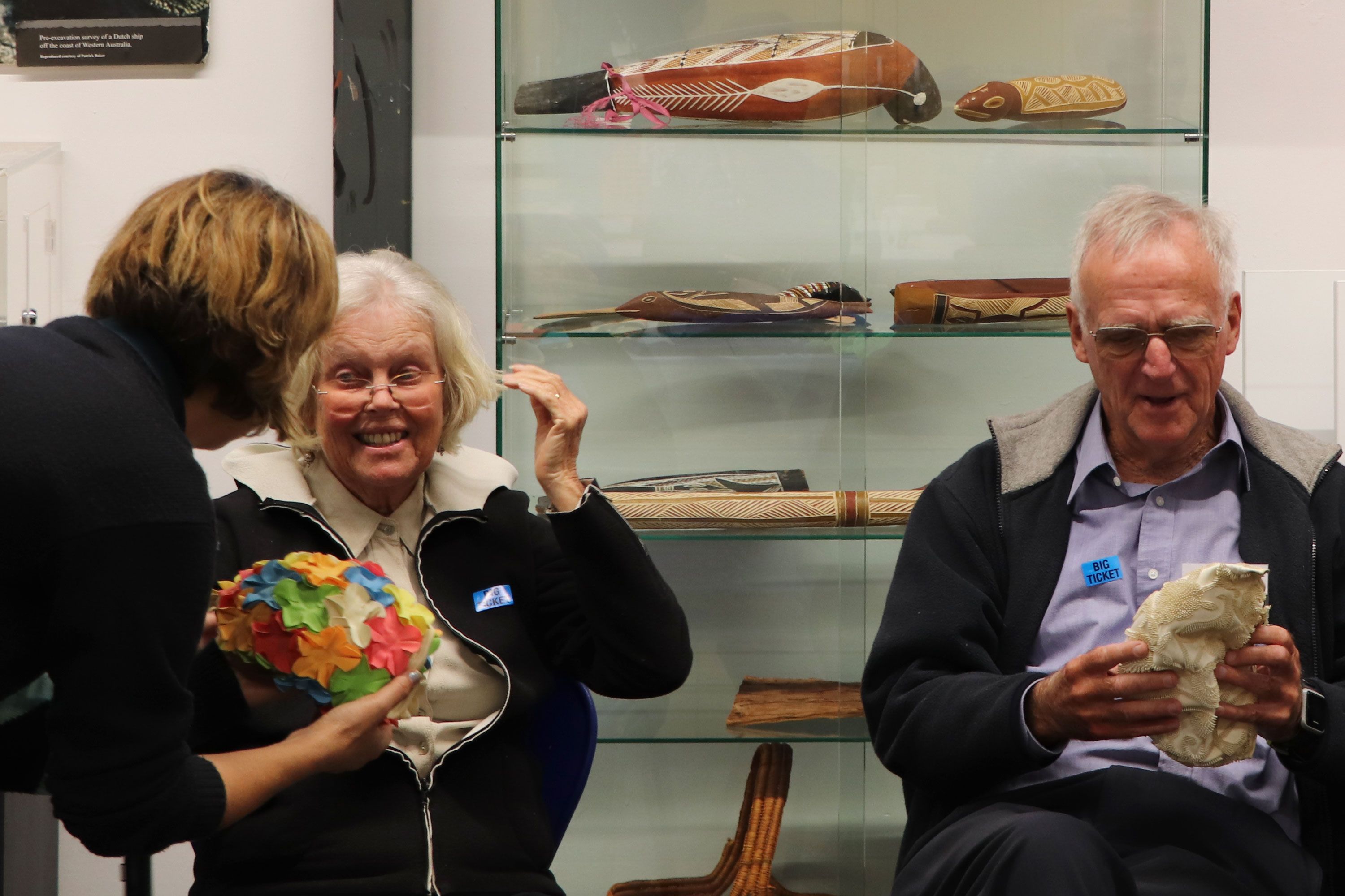 Photo of two older people, a man and woman, looking at bathing caps, talking to a museum staf member.