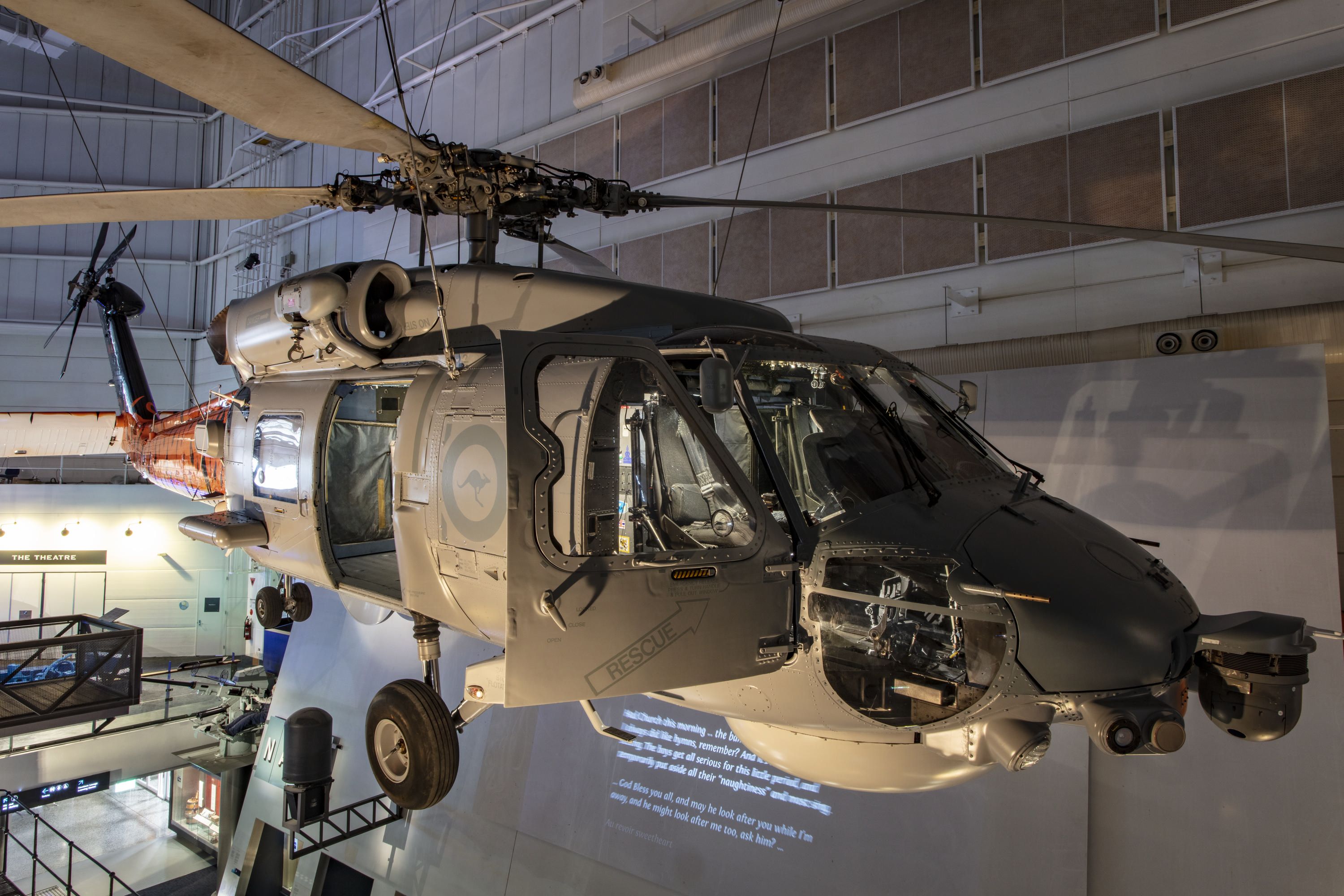 Milirary helicopter, mostly grey with orange and black tiger stripes painted on its tail, hung inside a museum gallery.  