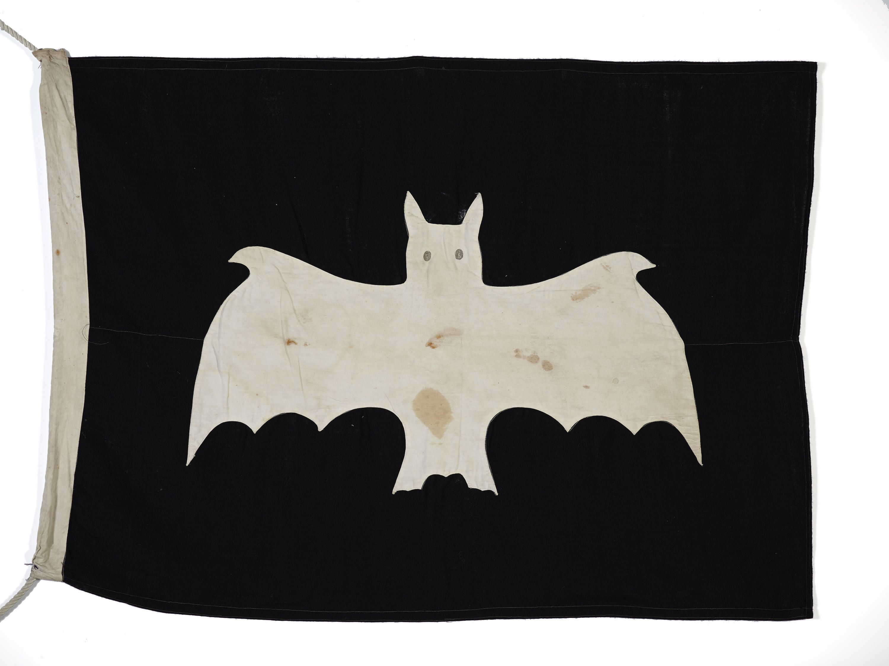 Photograph showing a black, rectangular flag with a white bat shape. 