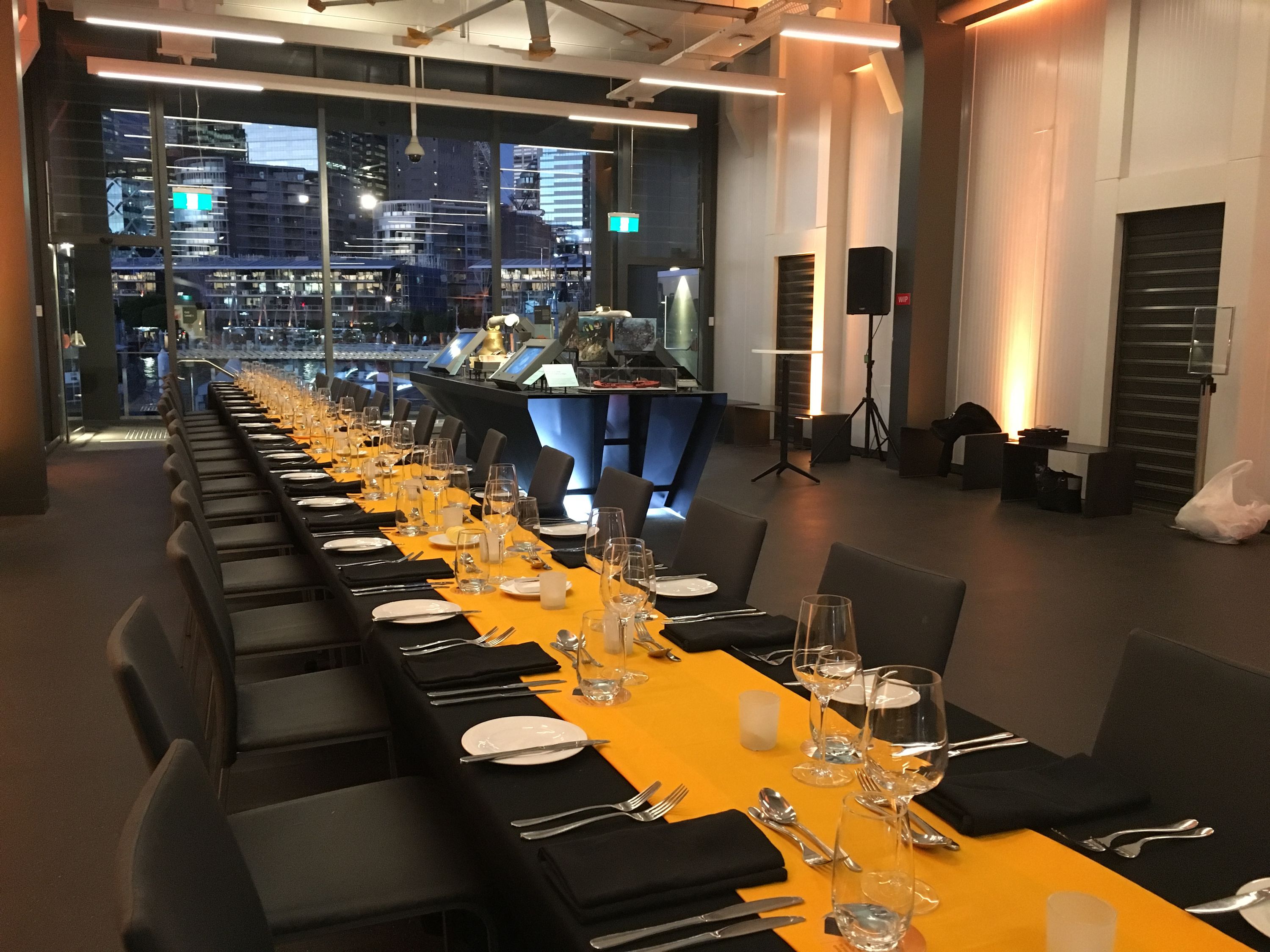 photo of an interior, with a long table decorated with a gold and black tablecloth and place settings. 
