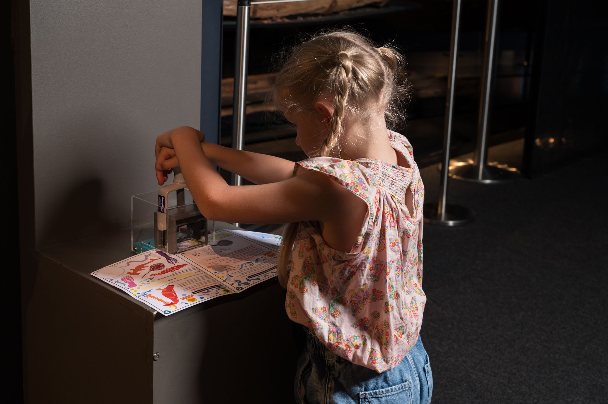 Photo showing a girl with blond plaits using a large stamp on an activity booklet.