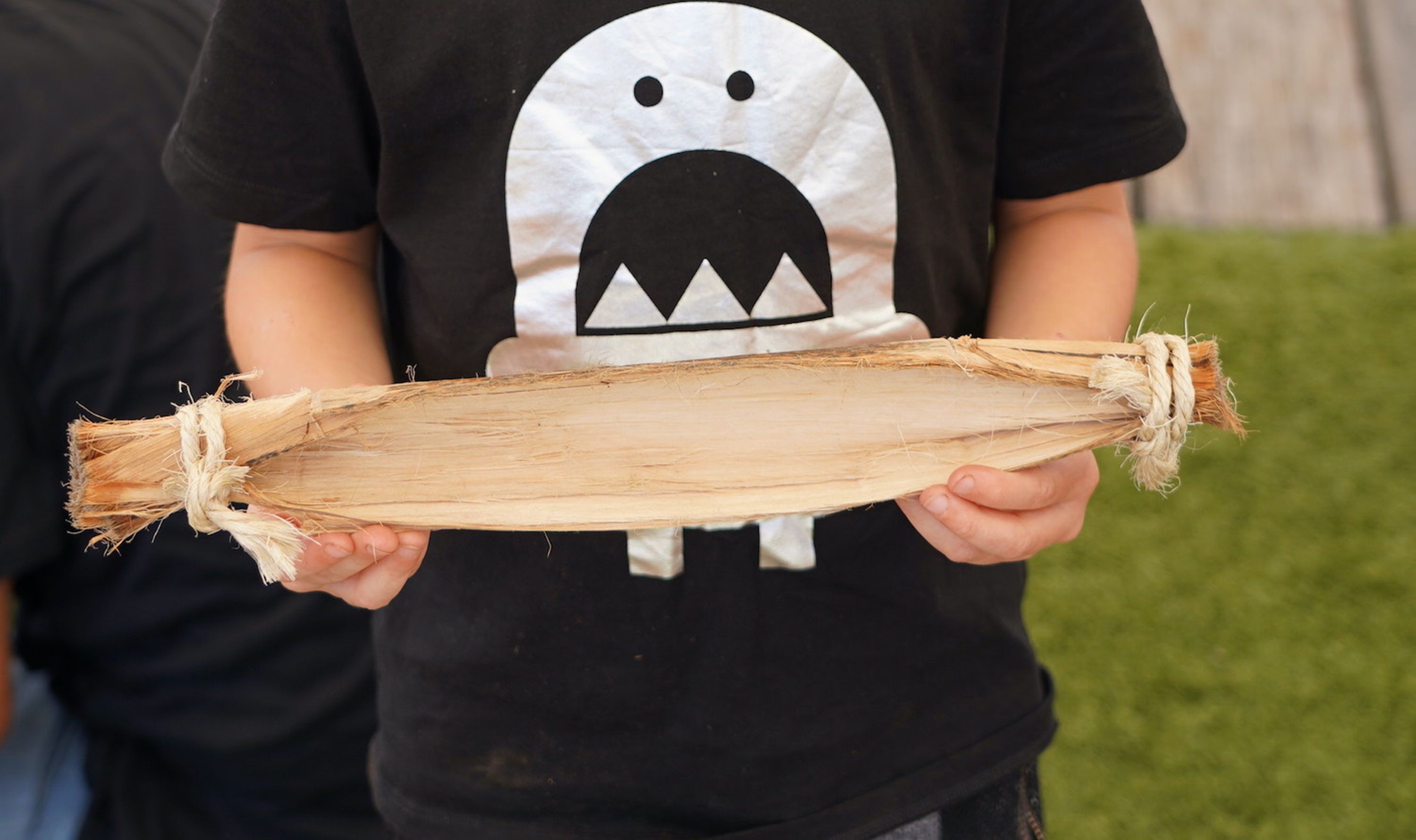 The torso of a boy with a black t-shirt holding a small model of a bark canoe, around 40cm long. 