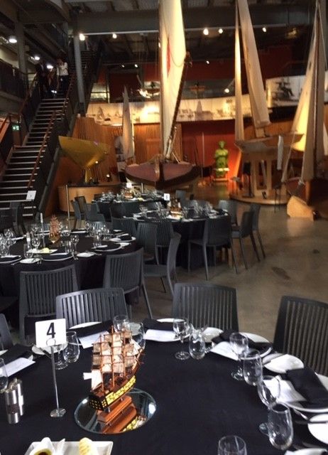 photo of event tables with set and decorated in front of wooden sailing boats. 