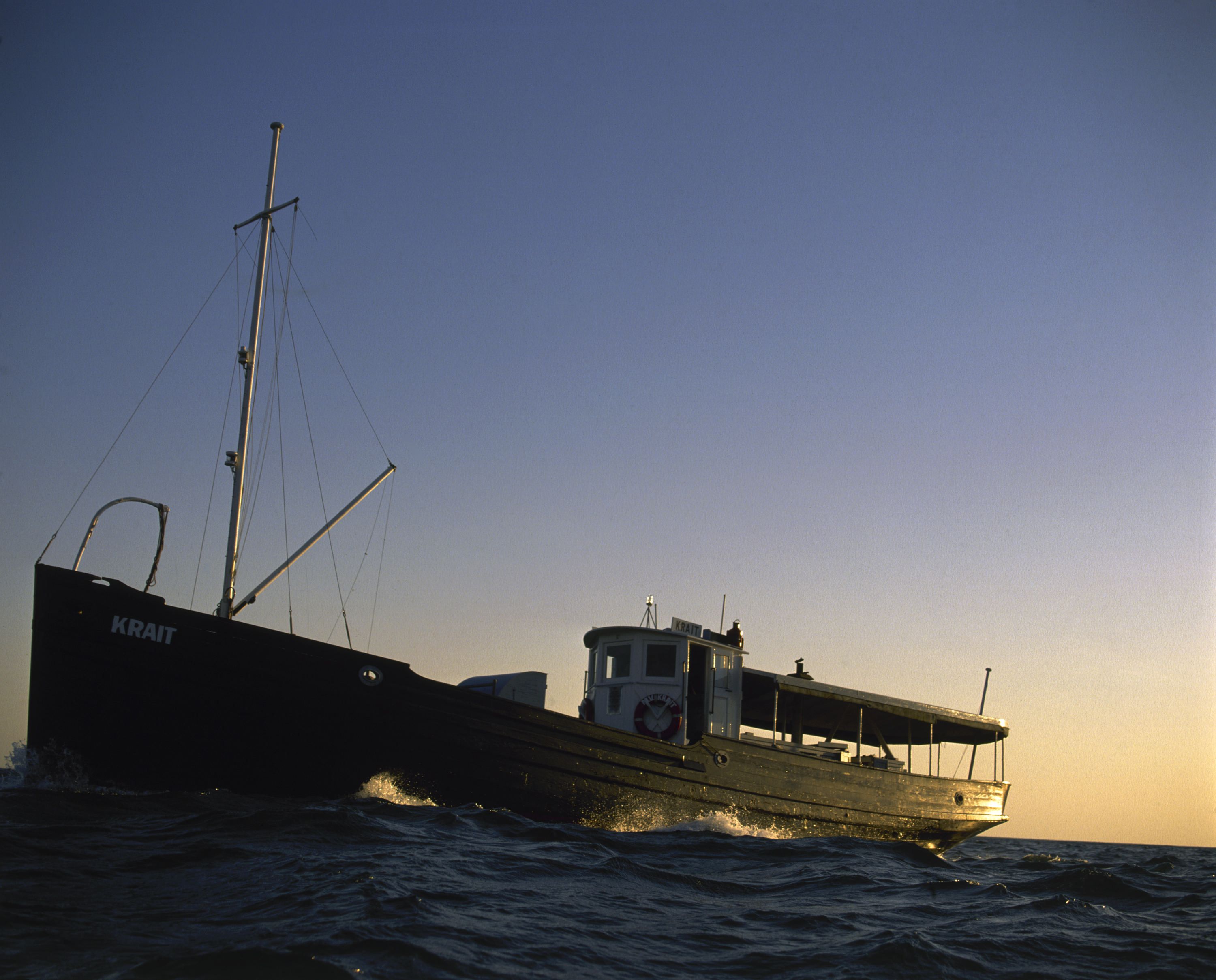 Photo of a dark coloured fishing boat with the sunrise or sunset behind it. 